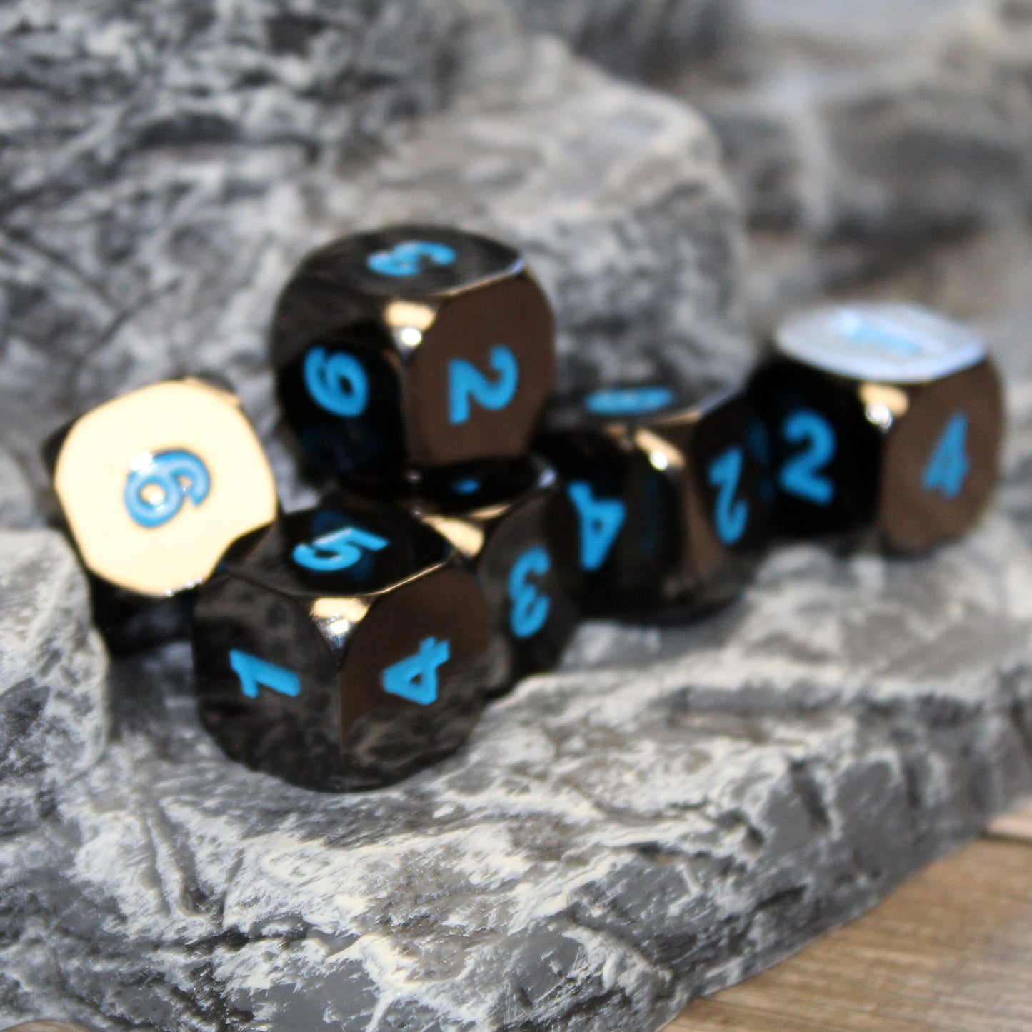 Six Black Frost D6 dice scattered on top of a rocky set piece