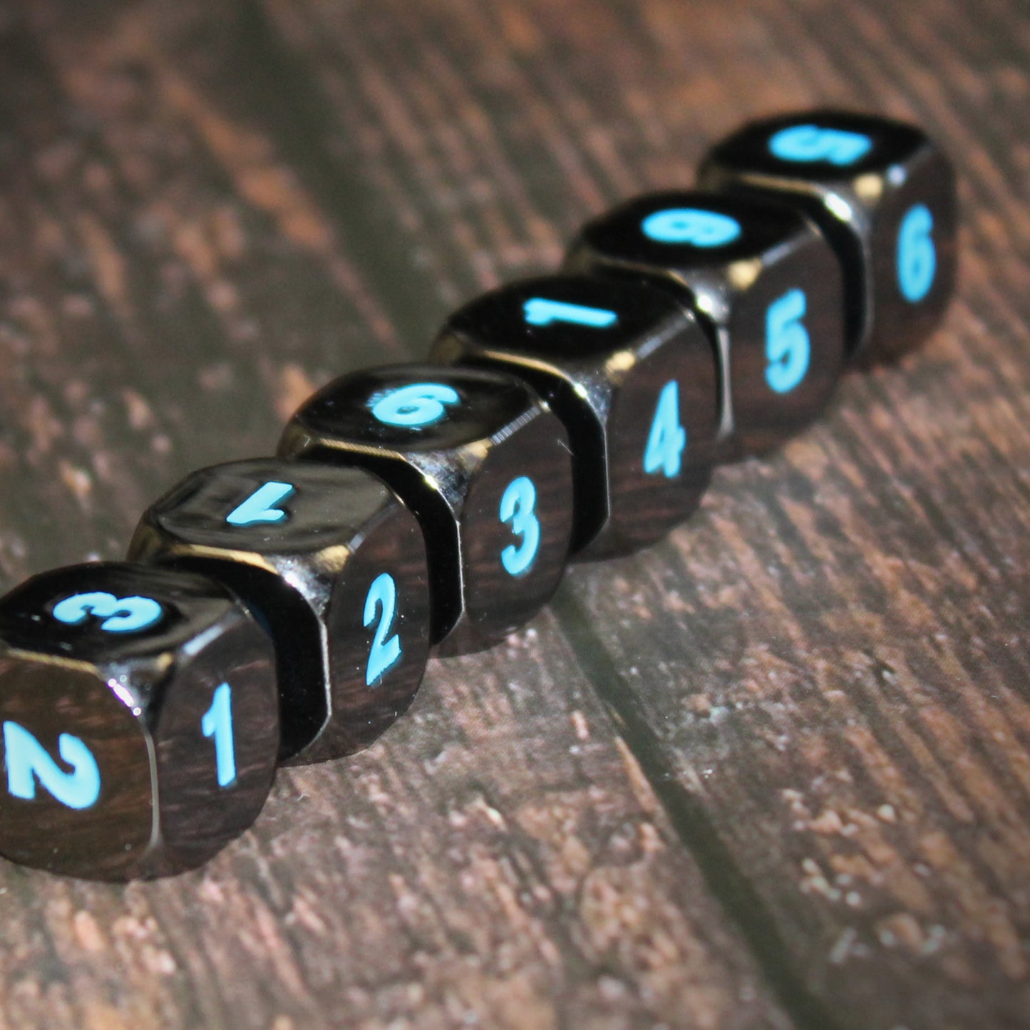 Black Frost D6 dice arranged in a line on a dark wood surface