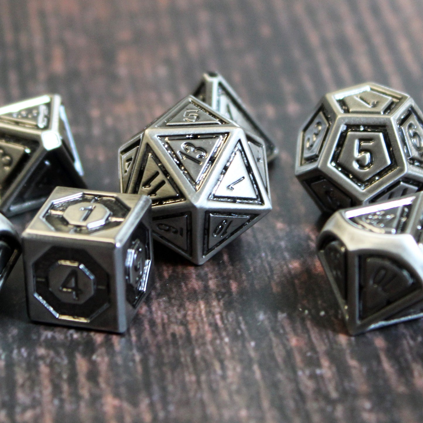Metal Bullseye dice set arranged in a scattered pile on a dark wood surface.