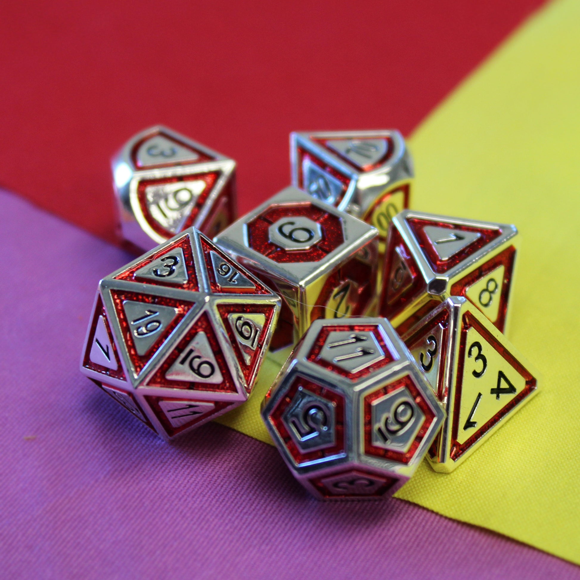 Metal BullsEye red dice set arranged on top of three squares of fabric, creating a background in which one third is red, one third is yellow, and one third is purple