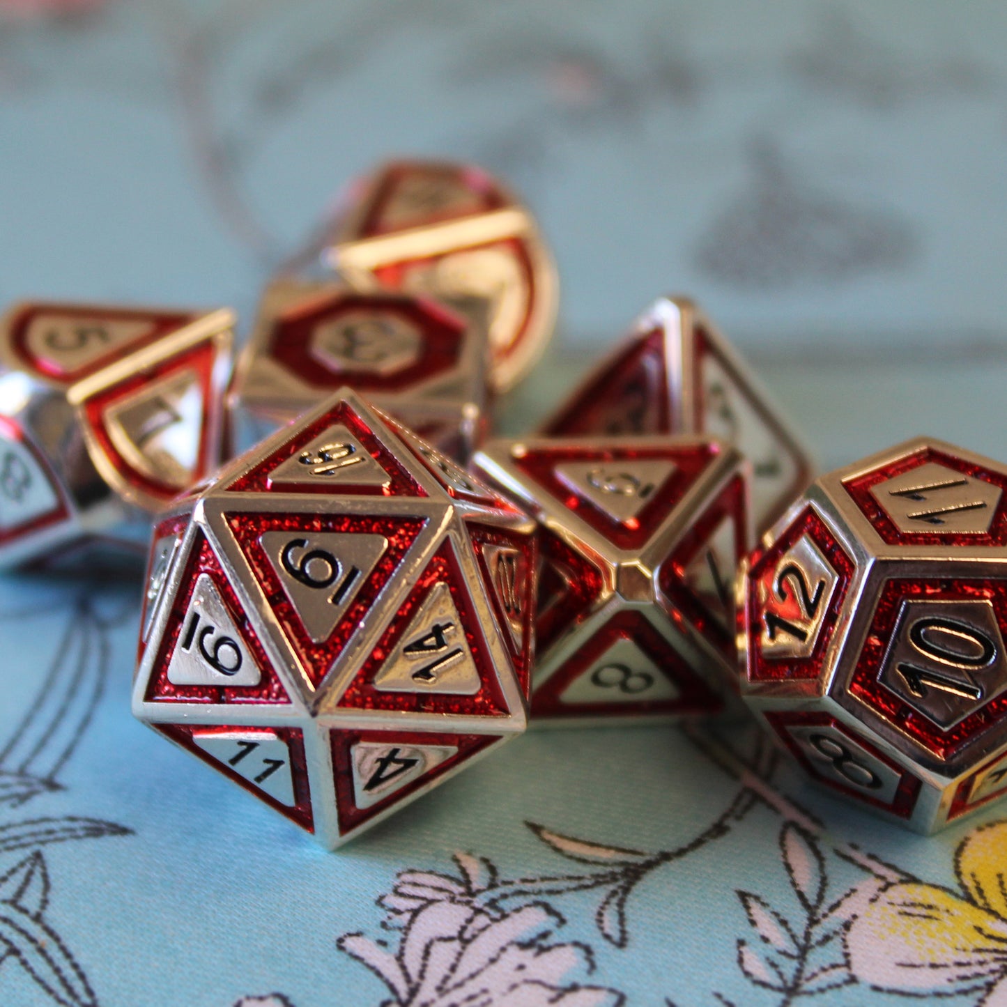 Close-up of Metal BullsEye red dice set arranged on top of a light blue fabric with white and yellow florals
