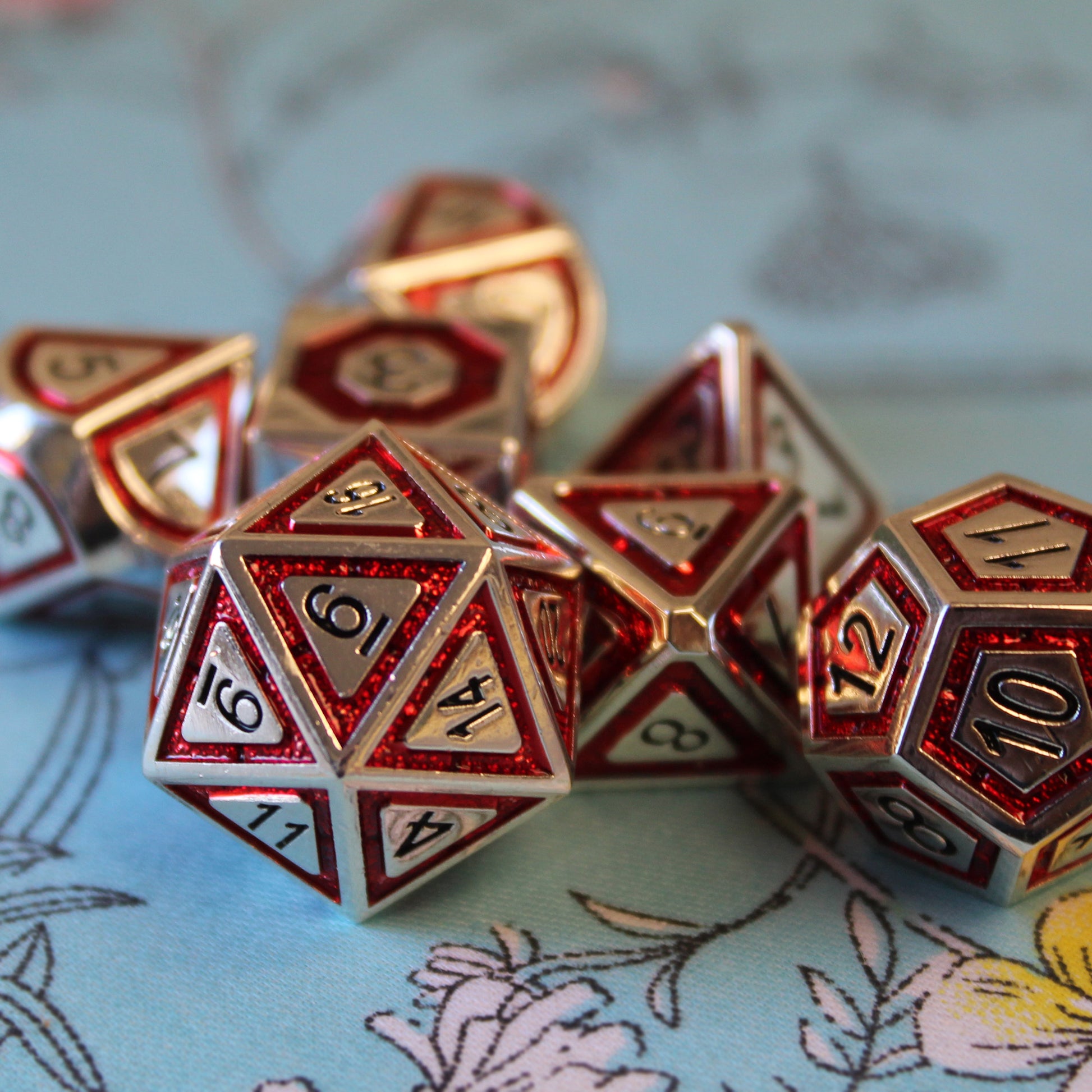 Close-up of Metal BullsEye red dice set arranged on top of a light blue fabric with white and yellow florals