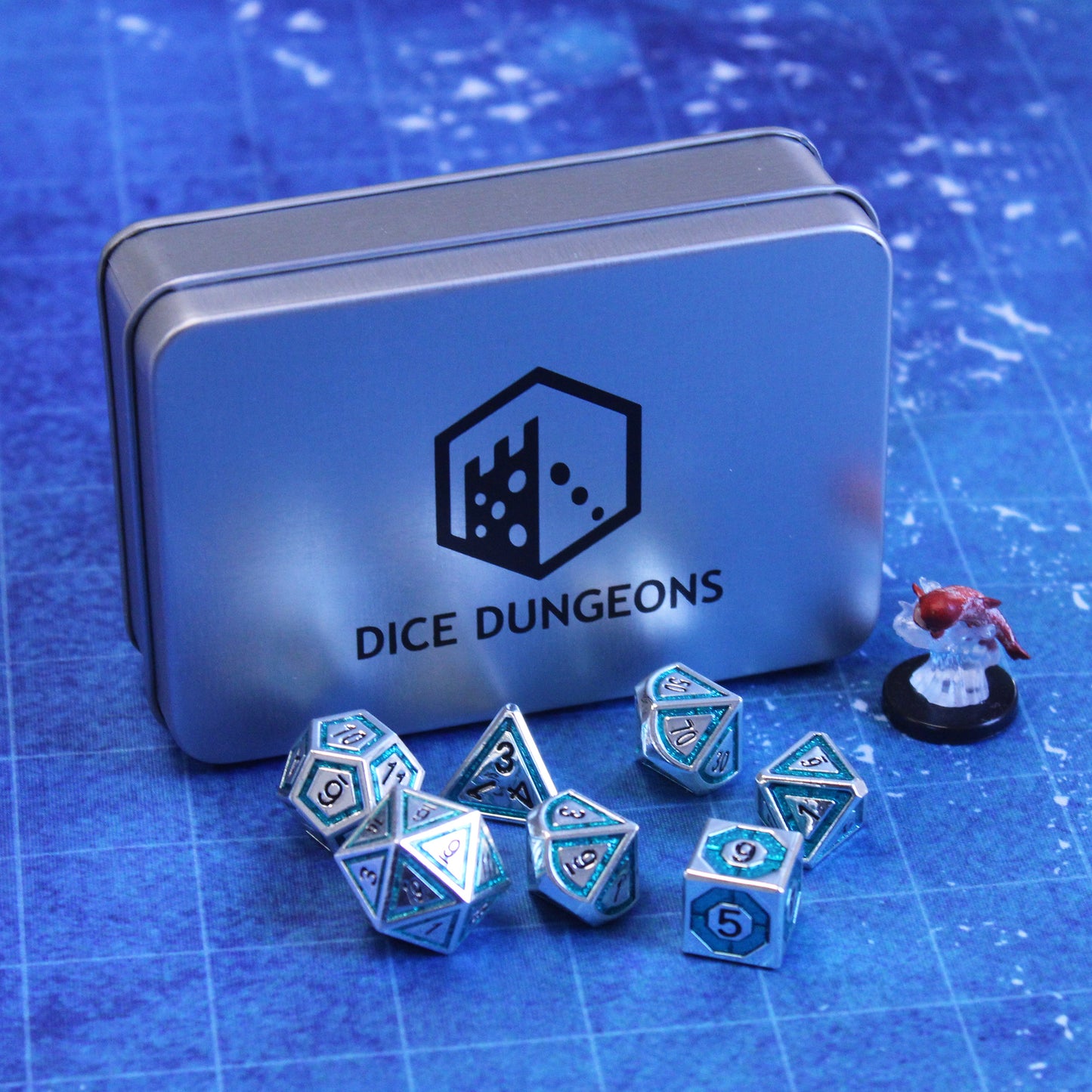 Photograph of silver gaming dice with teal inlays in a bullseye pattern on a blue gaming mat in front of a silver dice case with a figure of a fish nearby.
