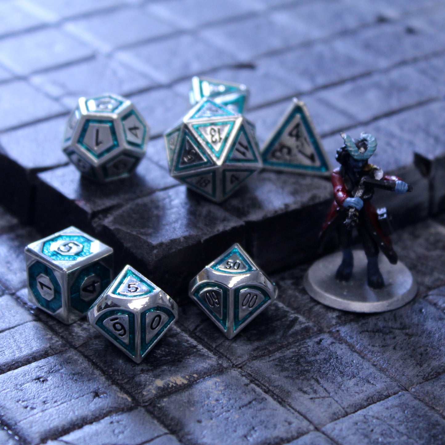 Photograph of silver dice with teal inlays on a grid next to a small figure of a horned being.
