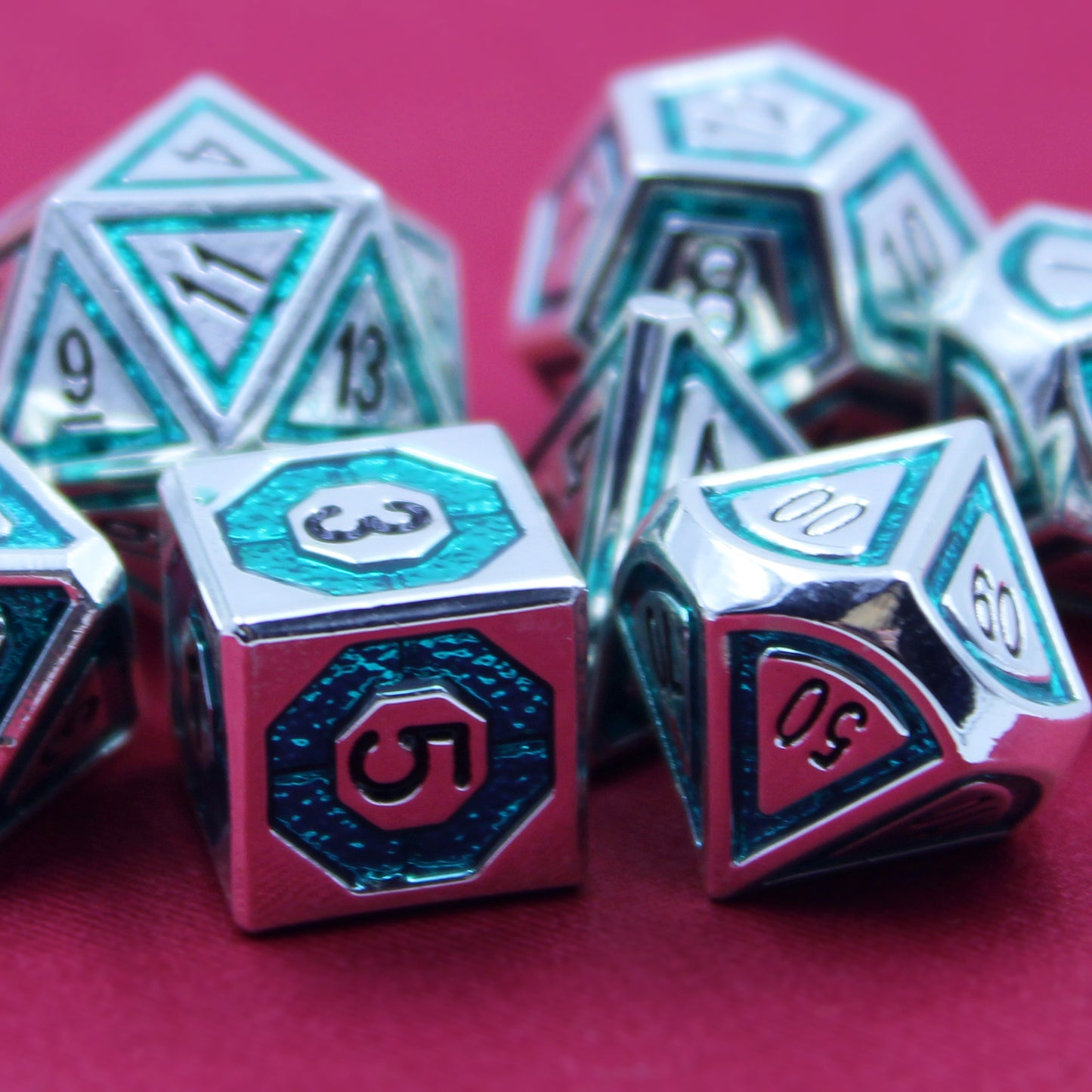 Closeup photograph of silver dice with teal inlays in a bullseye pattern on a red surface.