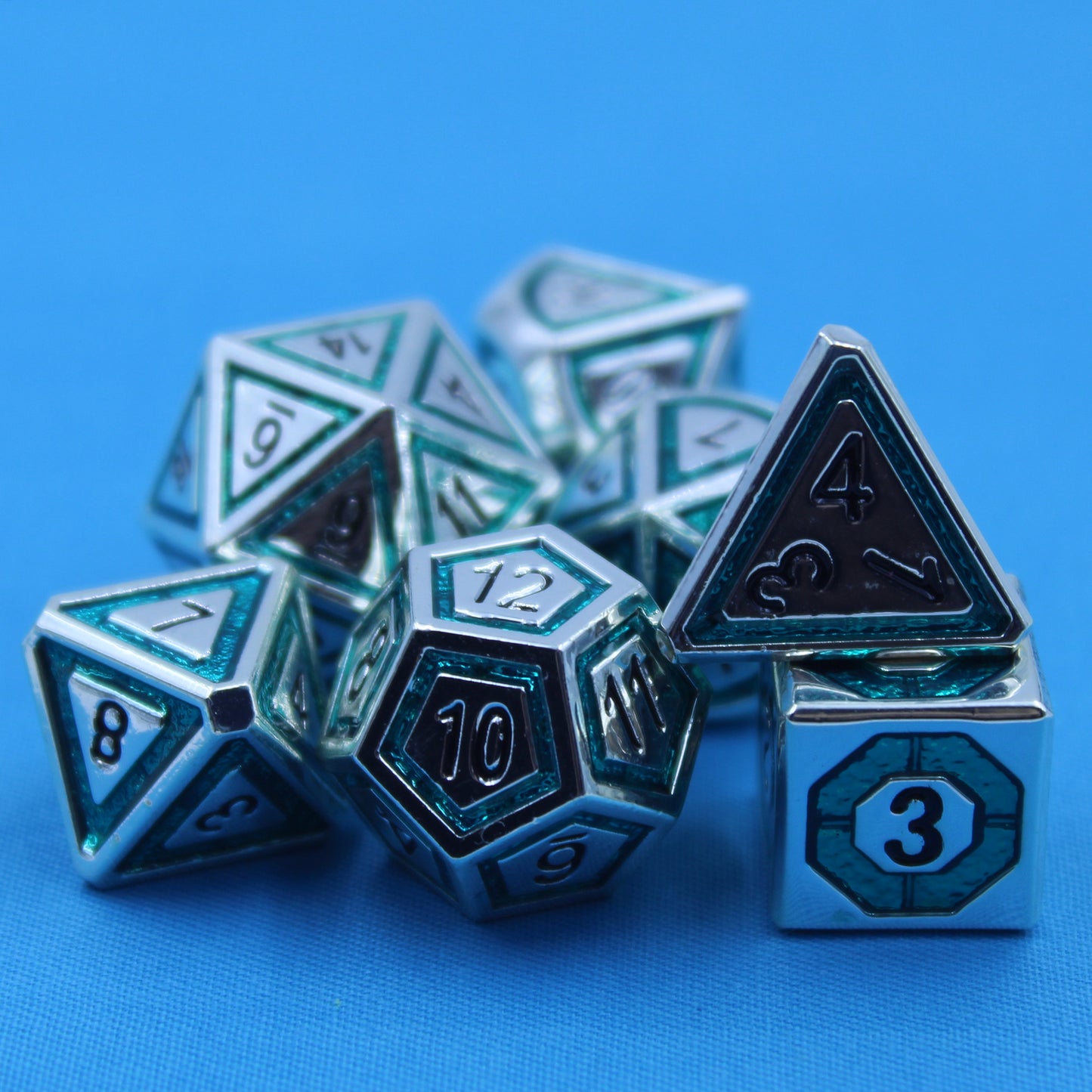 Closeup photograph of a set of silver dice with teal inlays in a bullseye pattern on a blue surface.