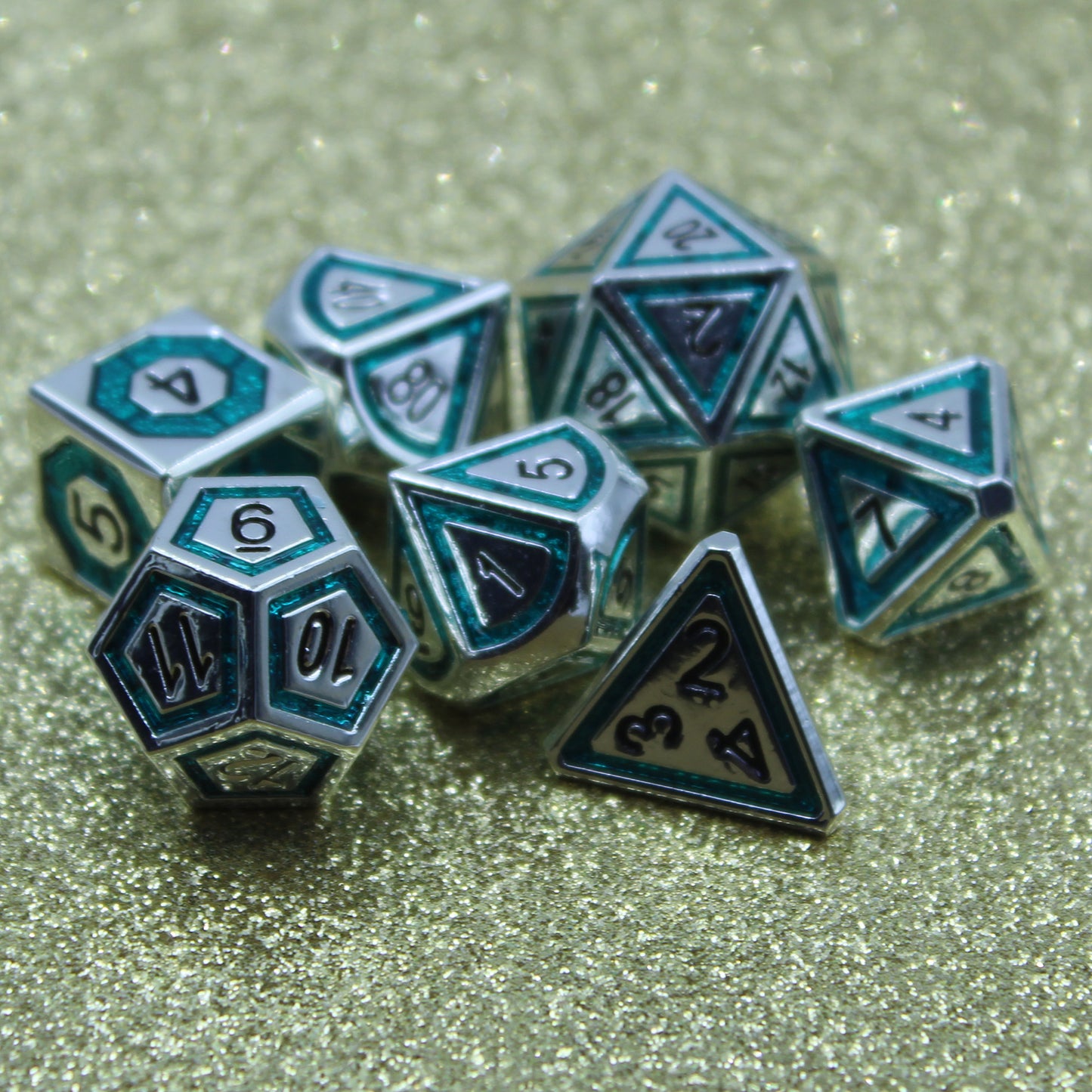 Closeup photograph of silver dice with teal inlays in a bullseye pattern on a glittery background.