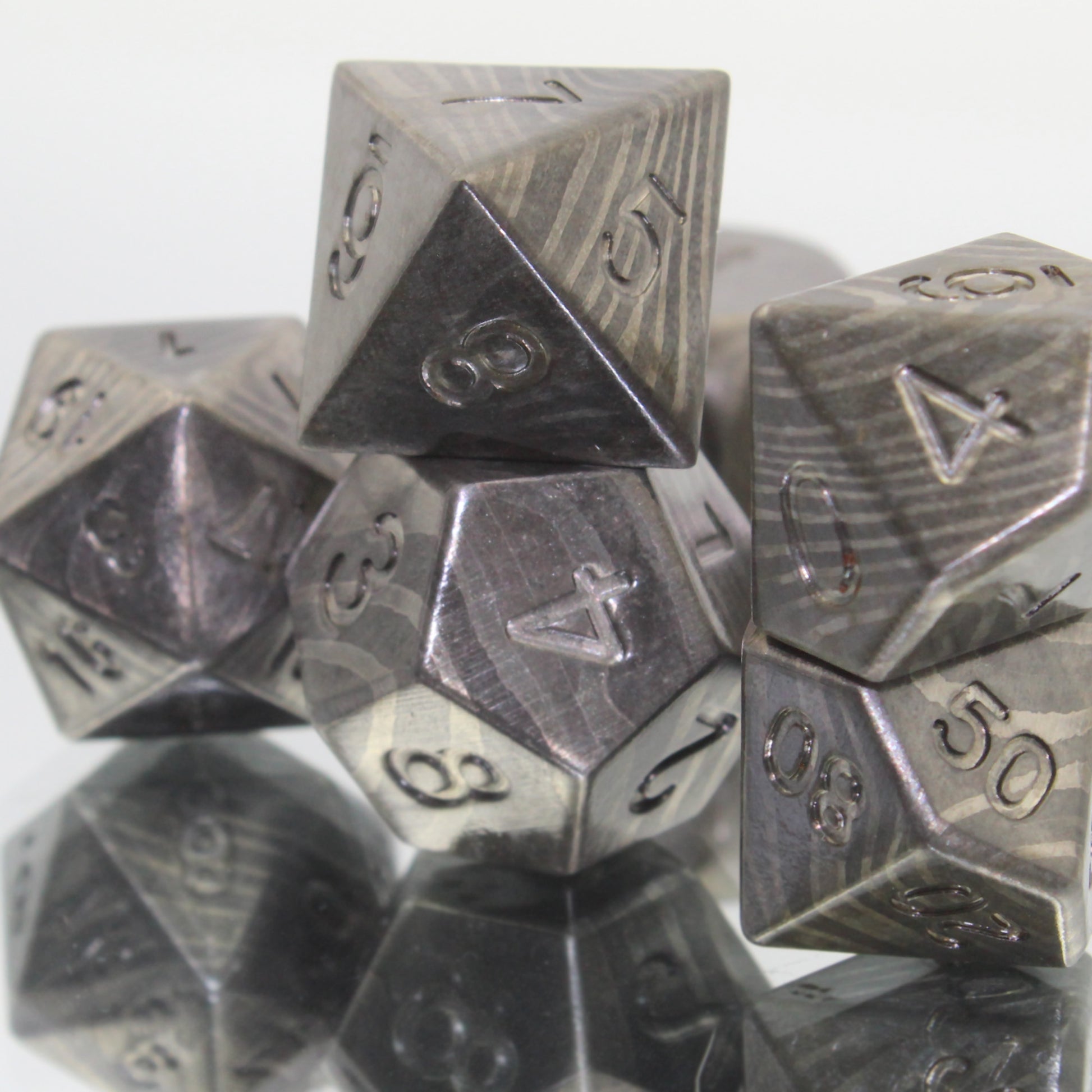 Closeup picture of the Metal Damascus Steel dice set highlighting the banding pattern of lighter and darker gray with the d12 central and the 4 face of that die towards the viewer.