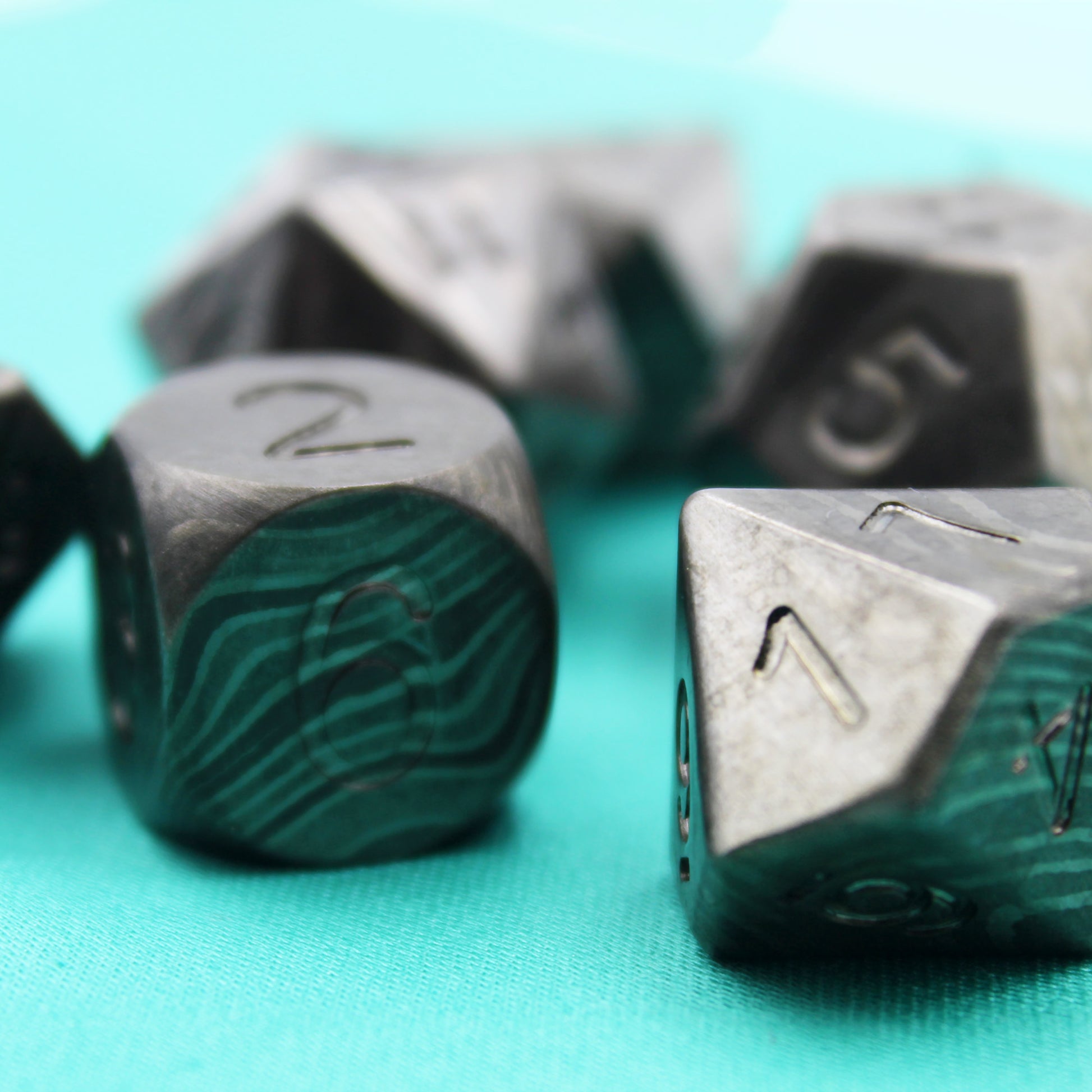 Closeup shot of the Damascus Steel dice set with the d6 and d10 in the foreground.  The d6 shows the 6 face and the d10 shows the 1 face, other dice from the set are in the background out of focus.