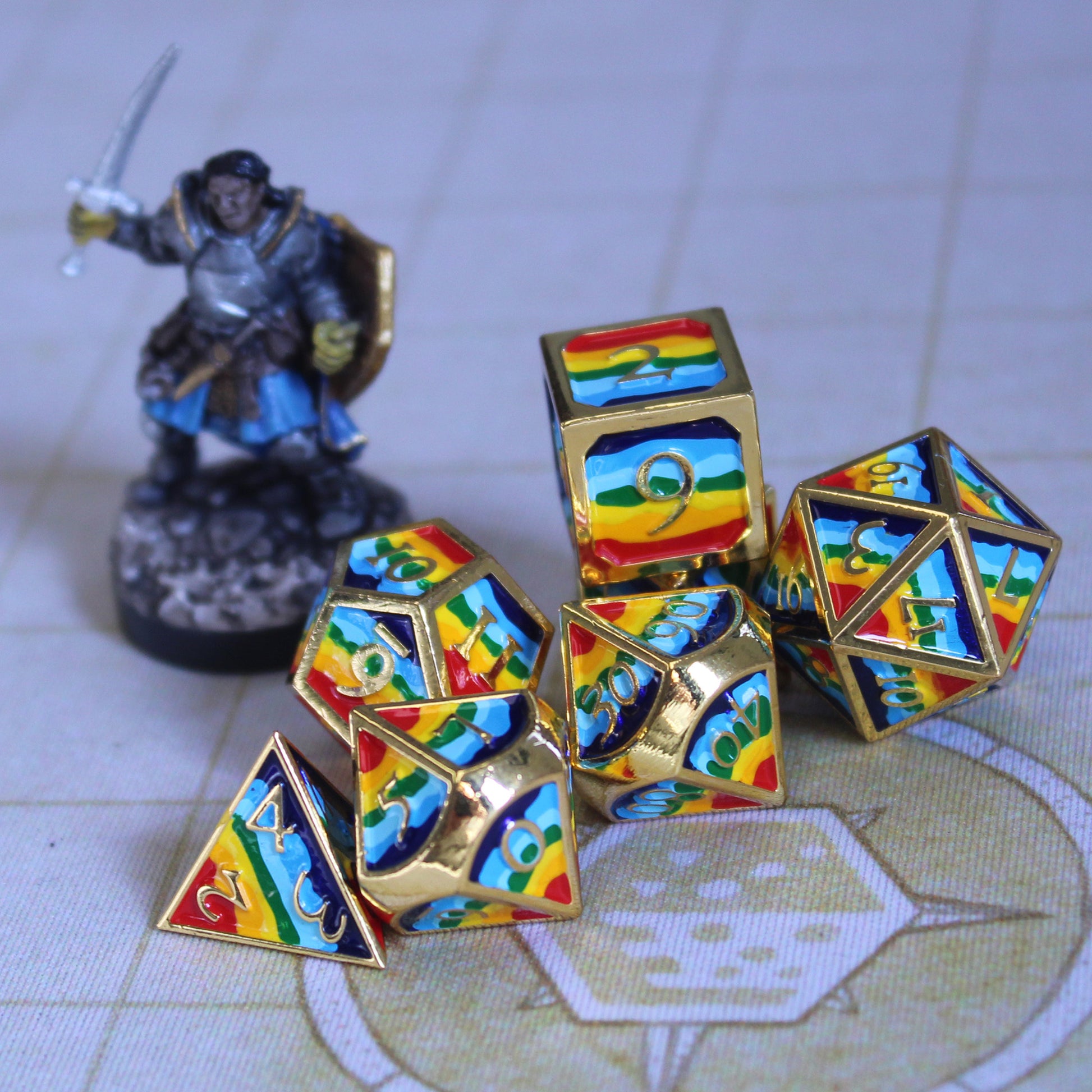 Photograph of rainbow-striped RPG dice with golden numbers and edges on a gaming mat next to a small armor-clad figure.