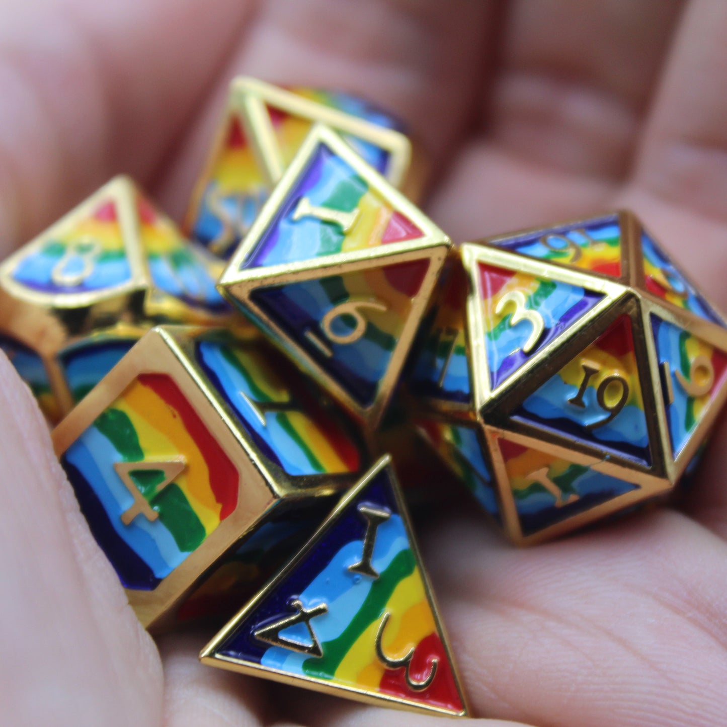 Closeup photograph of rainbow-striped RPG dice with golden numbers and edges in a person's palm.