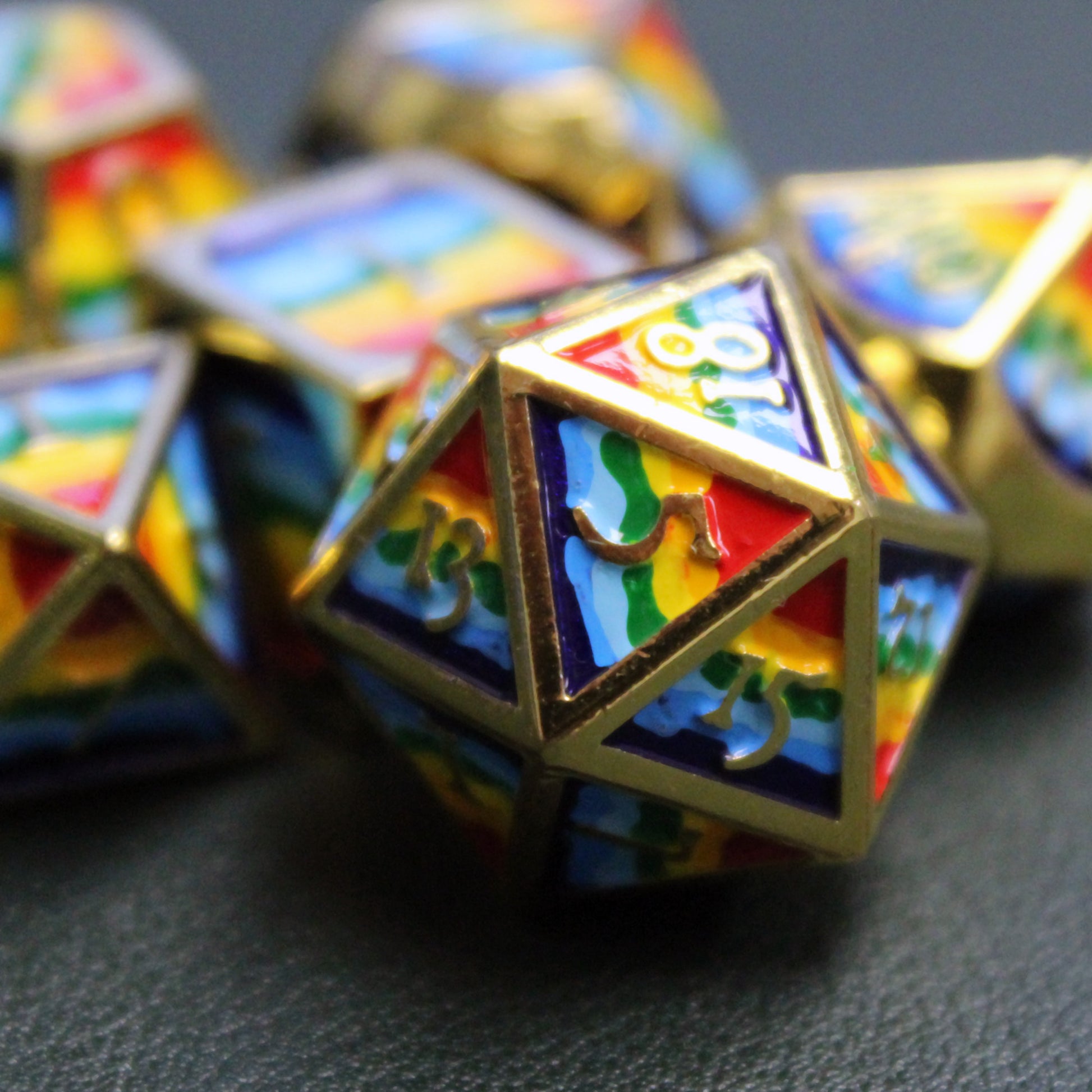 Closeup of rainbow-striped RPG dice with golden numbers and edges on a black surface.