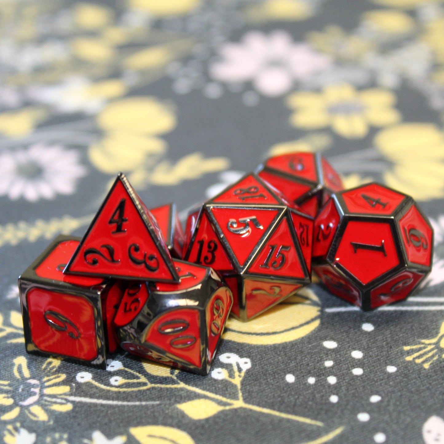 Metal Imperial Red dice set scattered on a black fabric with yellow and pink florals.