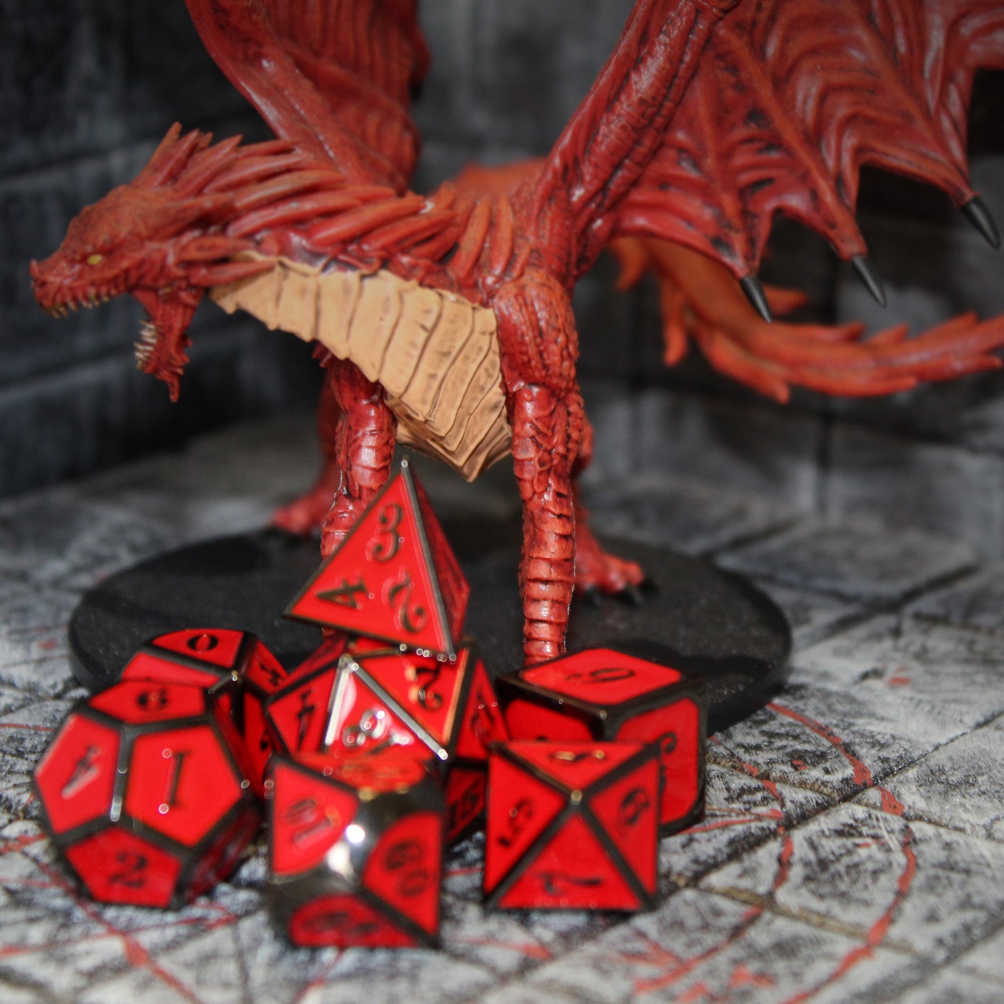 Metal Imperial dice set scattered in front of a red dragon figurine, on top of a stone floor game set.