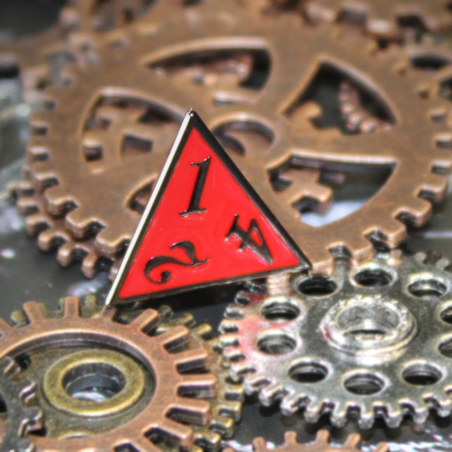 A close-up of the Imperial Red D4 die on top of silver and bronze gears