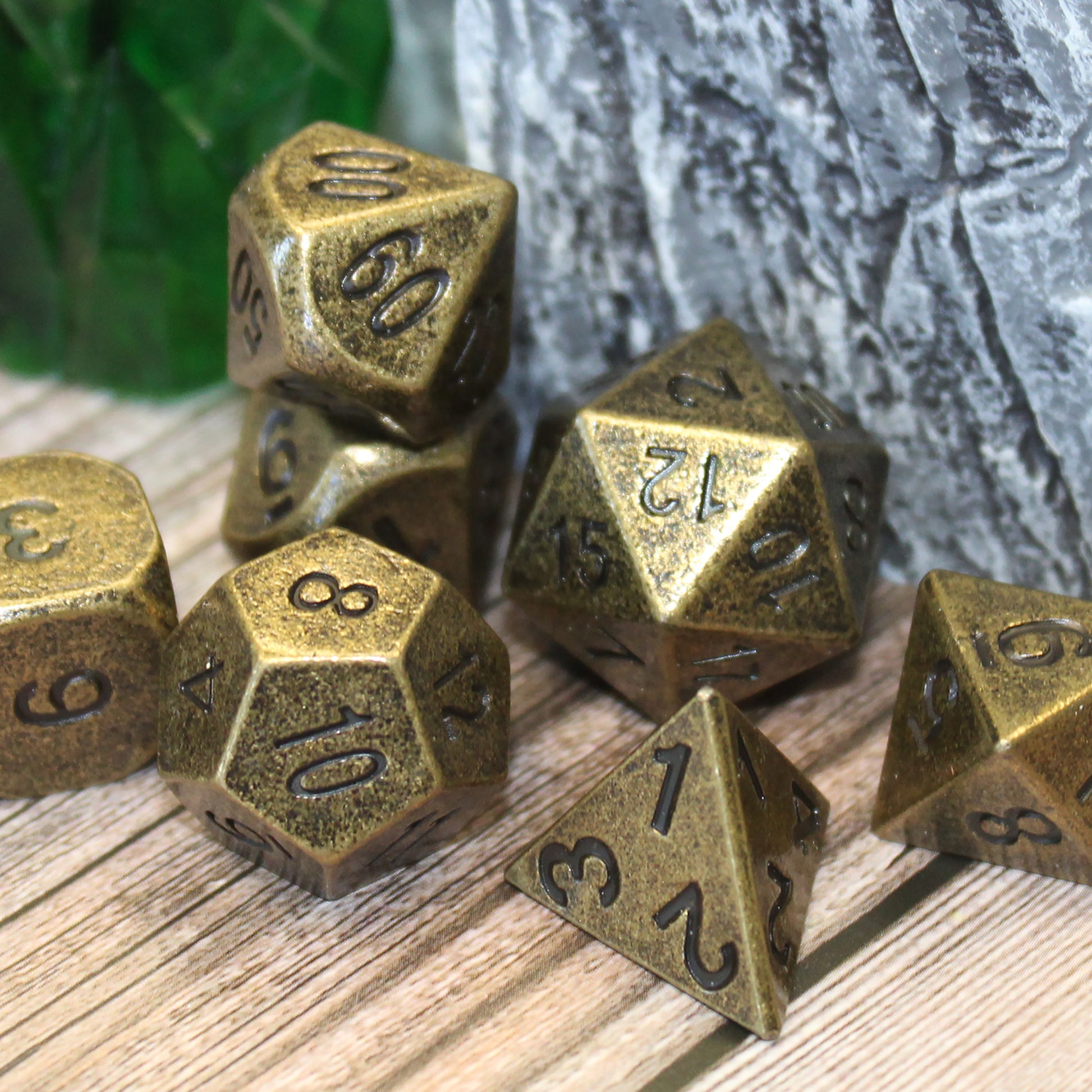 Primordial gold dice set scattered on a wooden surface with a rocky set piece behind them