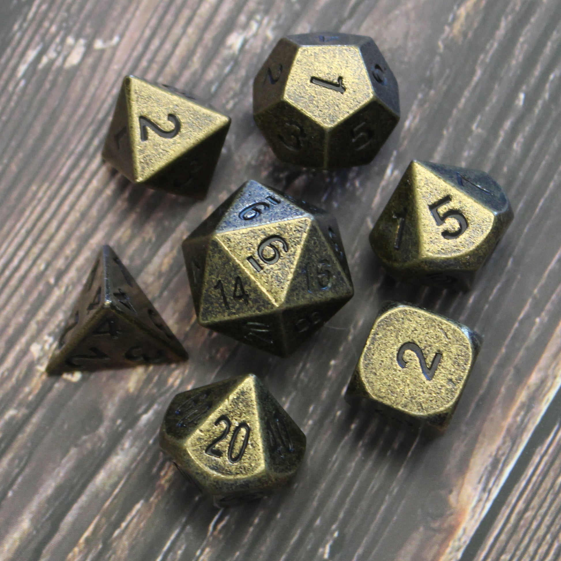 Primordial gold dice set arranged in a circle, with the D20 in the center and the other dice surrounding it, on a dark wooden surface