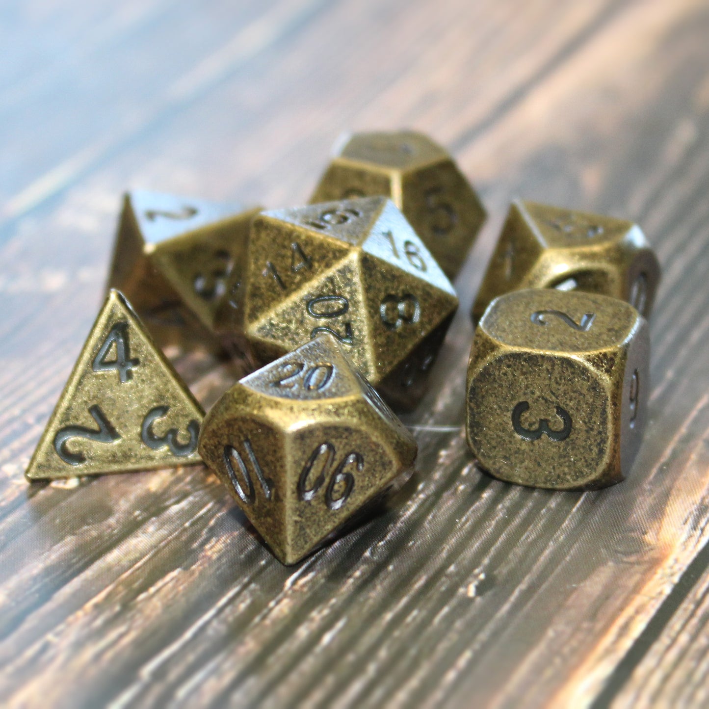 Primordial gold dice set arranged on a wooden surface. The dice display a tarnished gold appearance with black numbering.