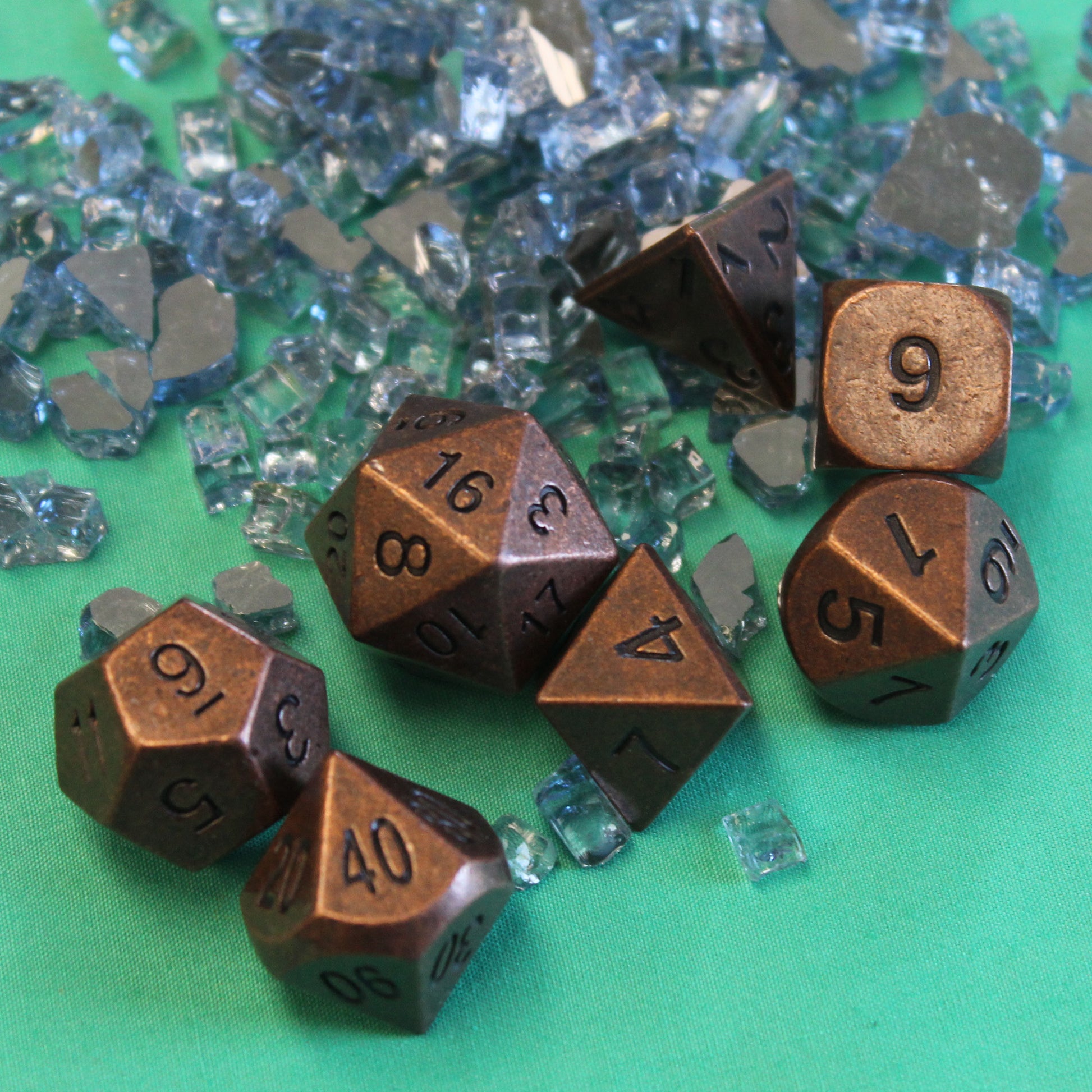 Primordial copper dice set arranged on a green fabric surface, with clear glass shards scattered around.