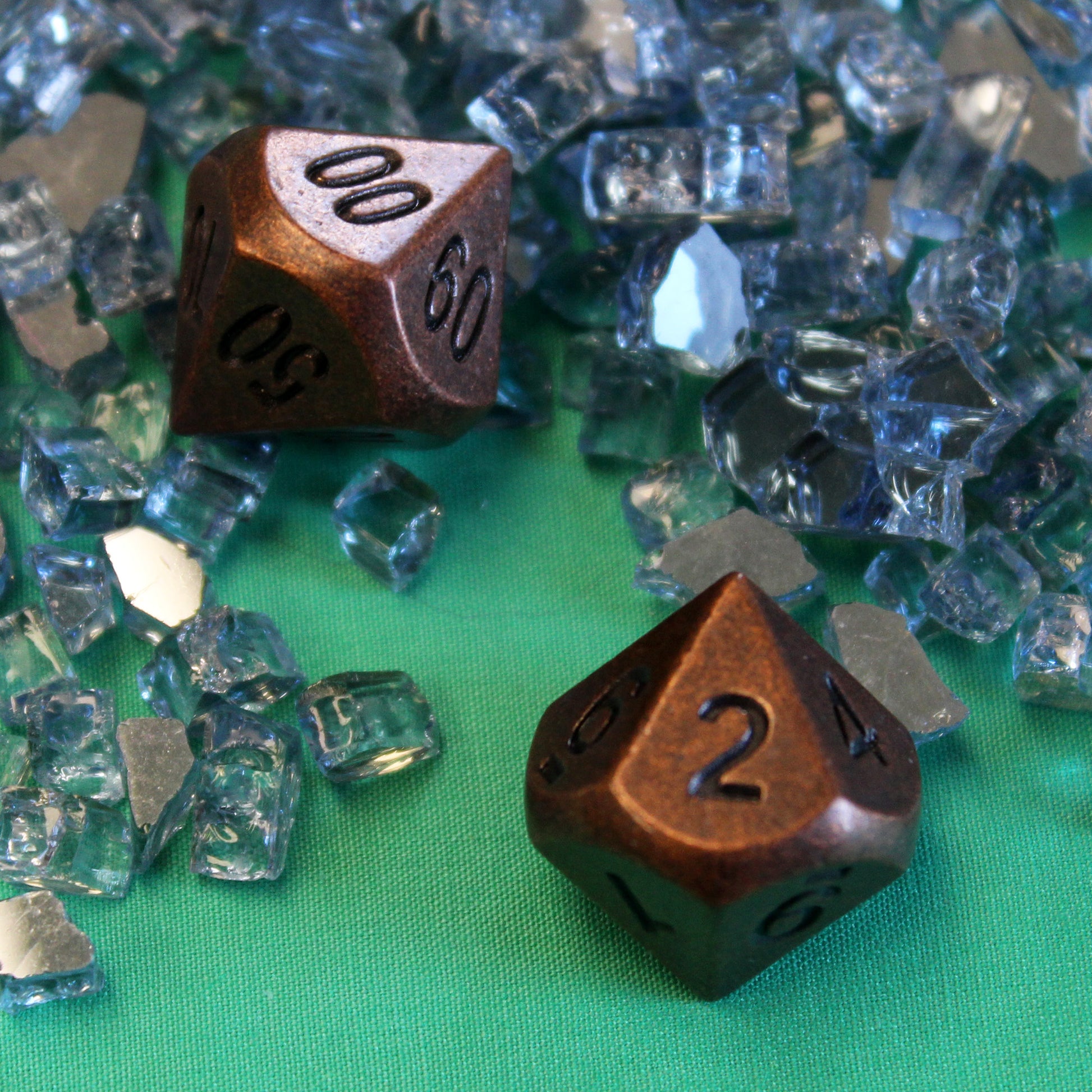 Two Primordial copper D10 dice on a green fabric surface, surrounded by clear glass shards