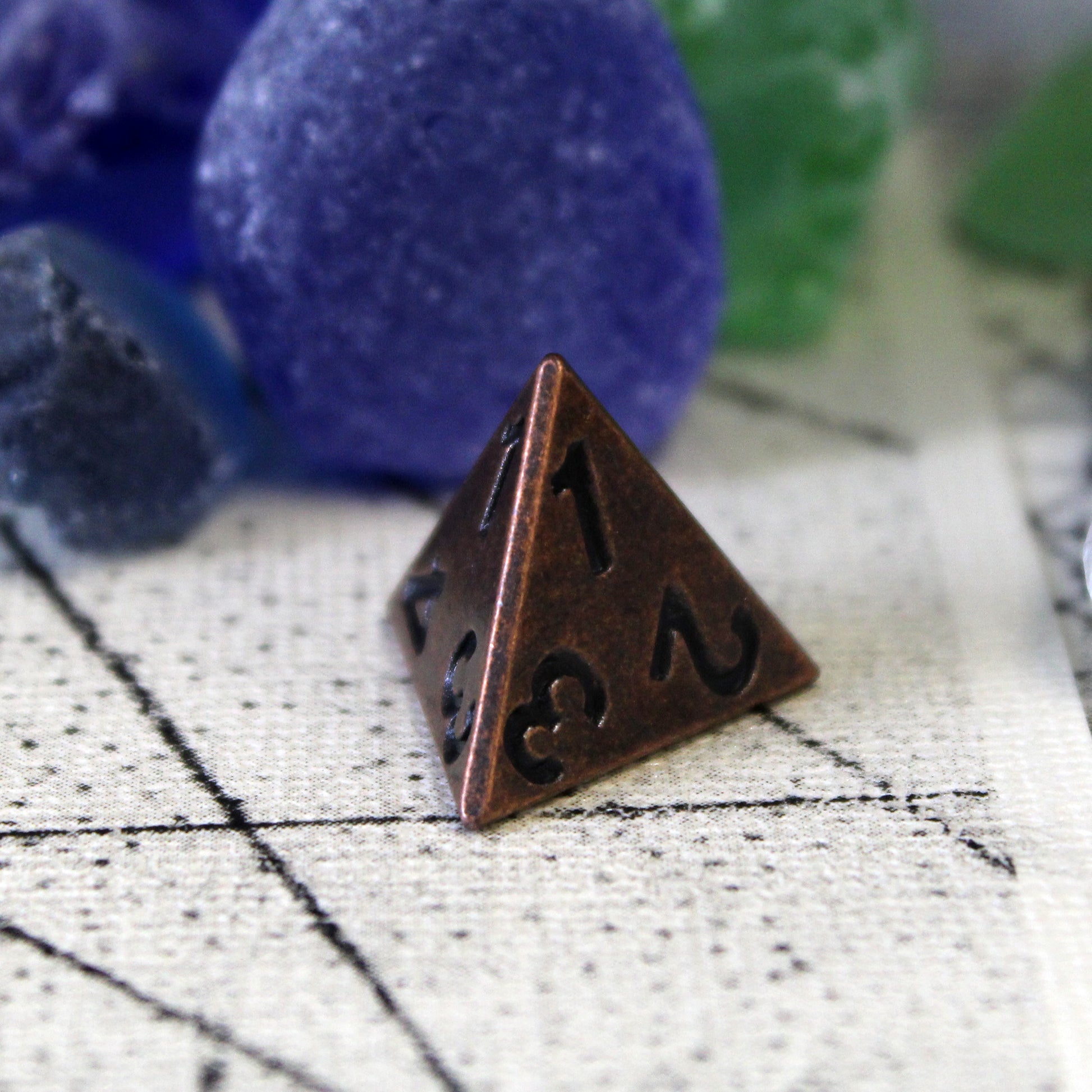 Primordial copper D4 on top of a tan play mat, with a variety of blue and green stones behind it