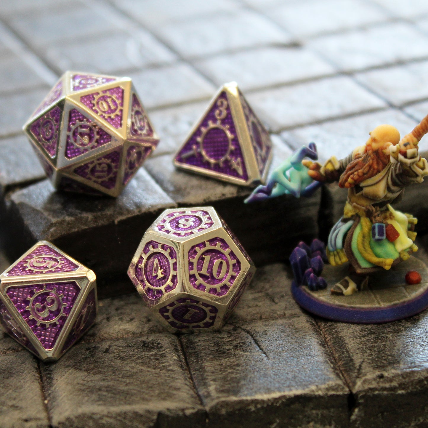 Four of the dice in the Mechanist set arranged on a rock tiled floor set piece with a mini figure to the right.