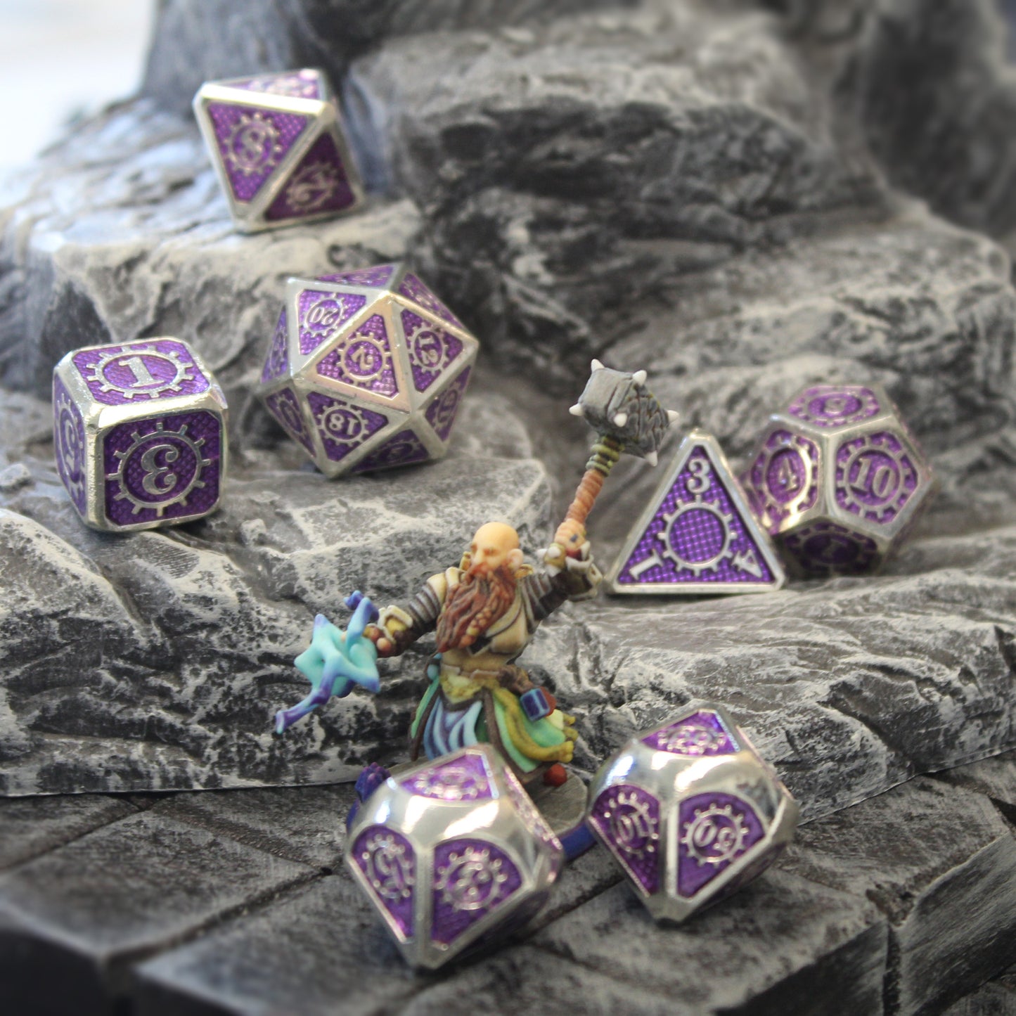 Mechanist dice set arranged on a rocky set piece with a mini figure wielding a weapon in front.