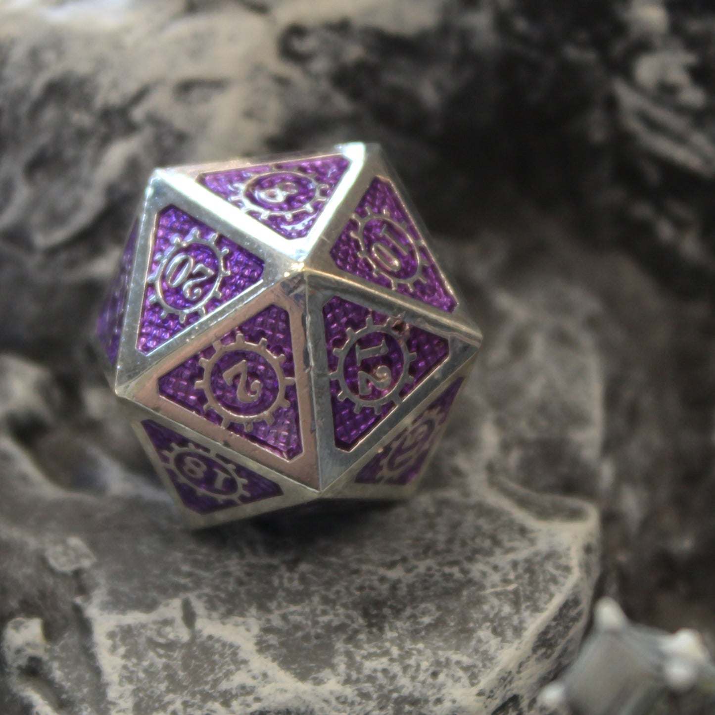 A closeup of the D20 from the Mechanist dice set on top of a rocky set piece.