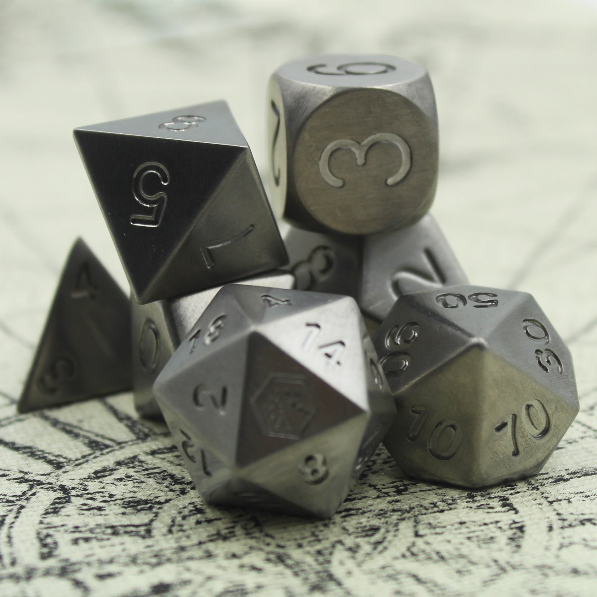 Metal Titanium dice set arranged in a pile on a white surface with a compass rose. The d8 and d6 rest atop in clear focus.