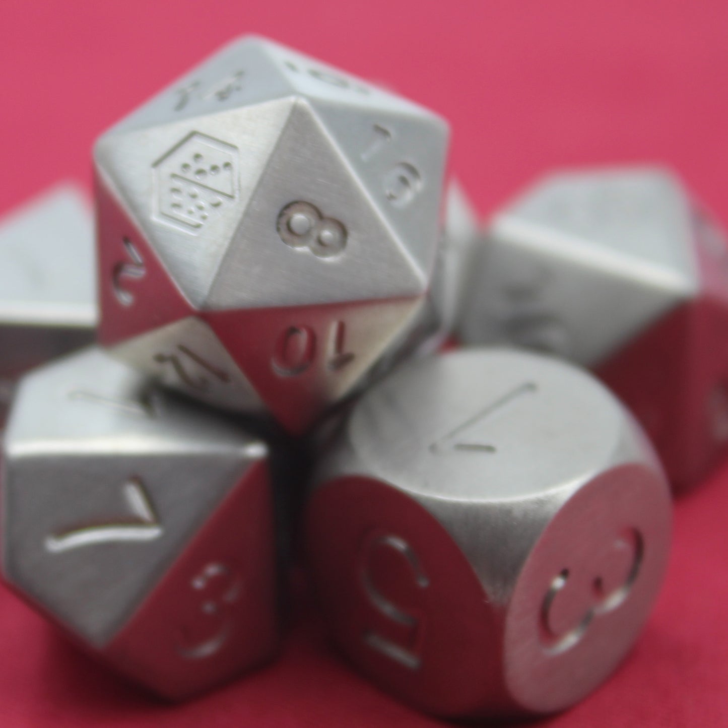 Closeup shot of the Metal Titanium dice set on a red background arranged in a pile with the d20 on top.  The 8 face of the d20 is towards the viewer.
