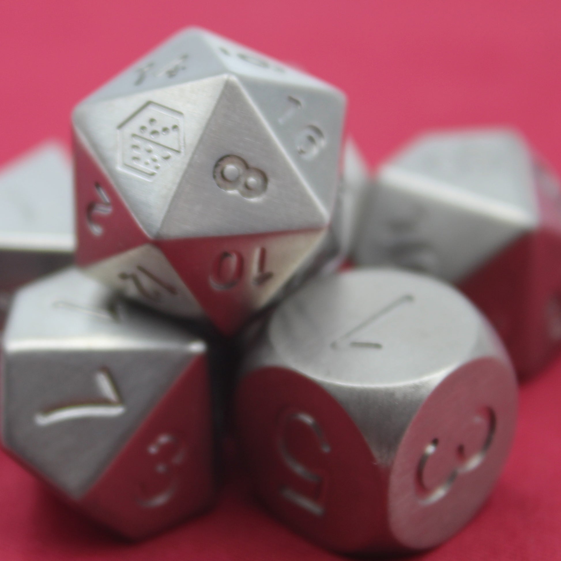 Closeup shot of the Metal Titanium dice set on a red background arranged in a pile with the d20 on top.  The 8 face of the d20 is towards the viewer.