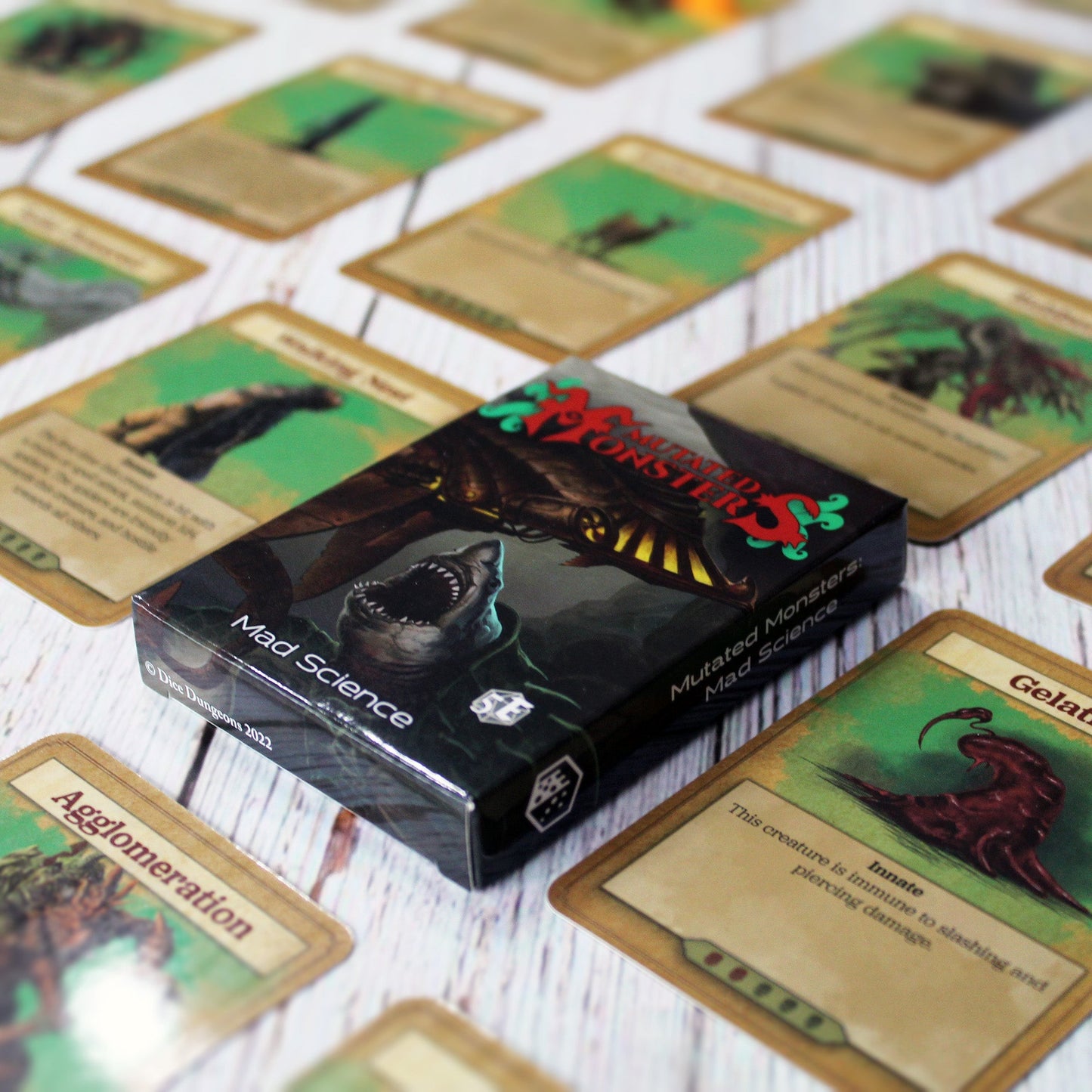 Deck box in the center of the image with individual cards from the deck spaced out equidistant from each other in a repeating pattern, all on a white wood paneled background.