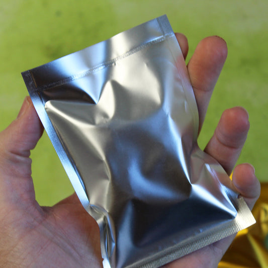 Silver foil bag in the palm of a person's hand, a lime green background behind them.