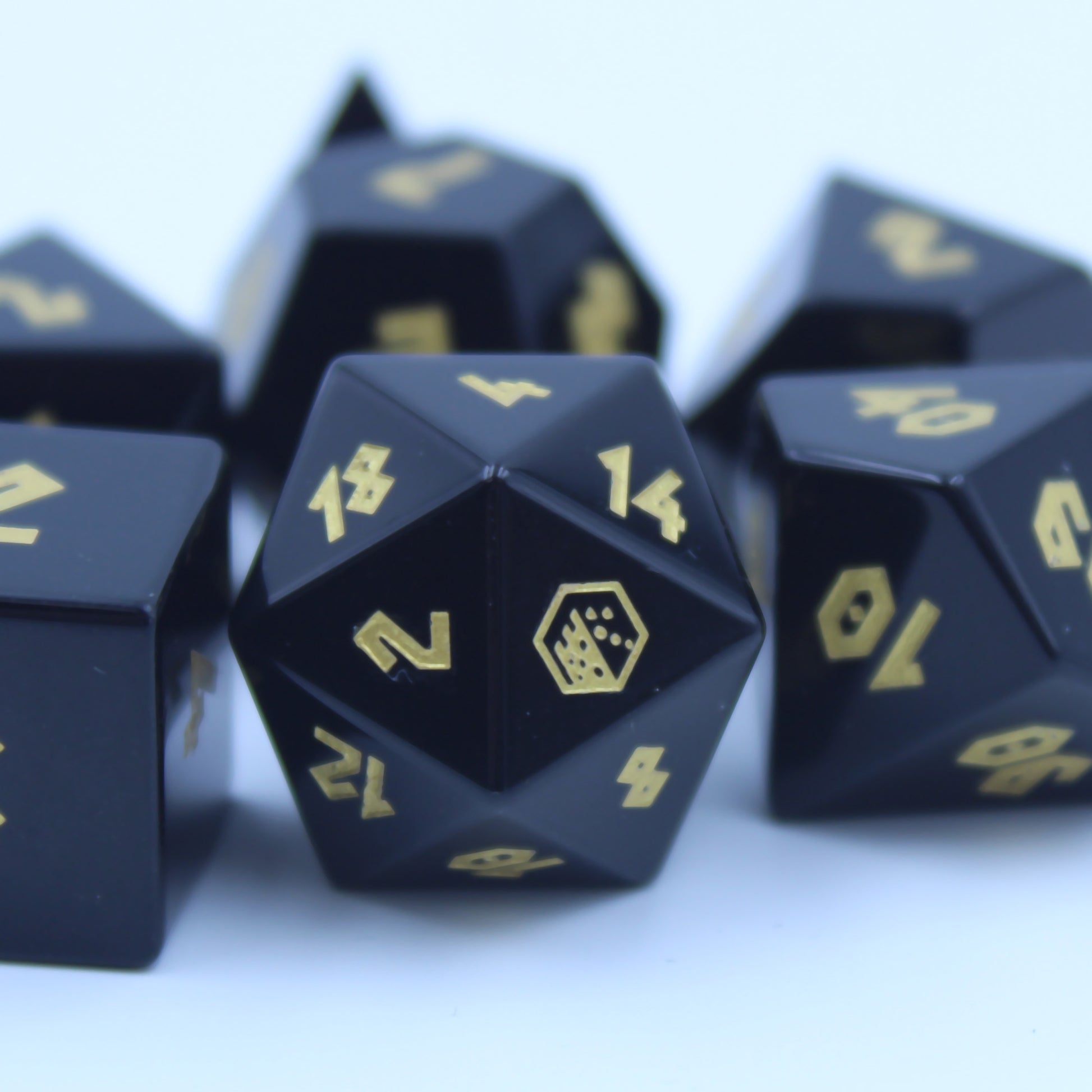 Close-up of D20 die with jet black obsidian and bright gold numbering, featuring the Dice Dungeons logo as the 20 for a unique DnD touch.