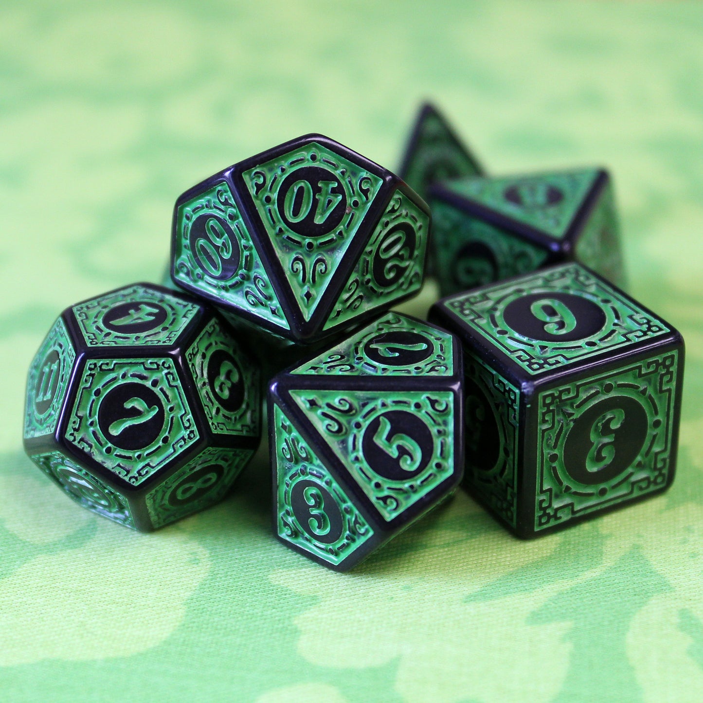 Oracle's Flame green dice set arranged in a pile on top of a two-toned green patterned cloth.