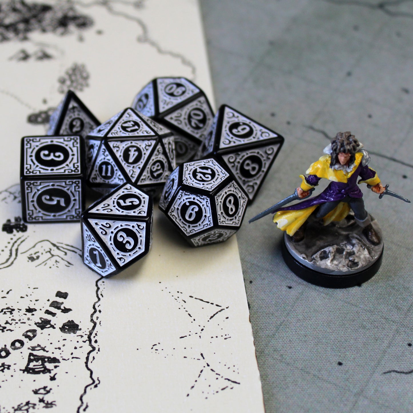 Oracle's Flame white dice set arranged in a pile on top of a white and gray game map. To the right of the dice pile there is a mini figure.