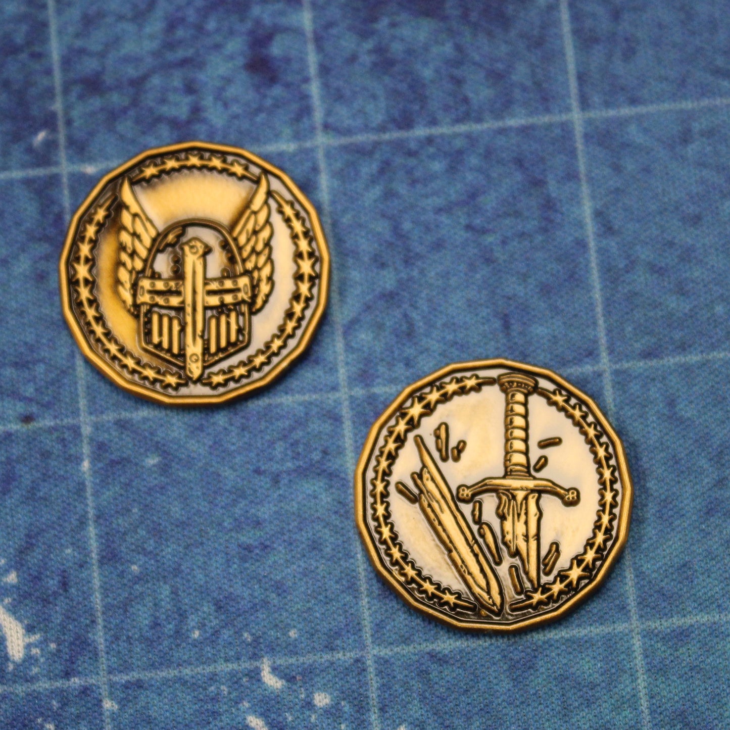 Two antique gold finished Paladin Character coins arranged on a printed map surface. The coins are flipped to opposite sides, one coin displaying the winged helmet and the other coin displaying the broken sword. These coins are sized for a 1 inch battle map.