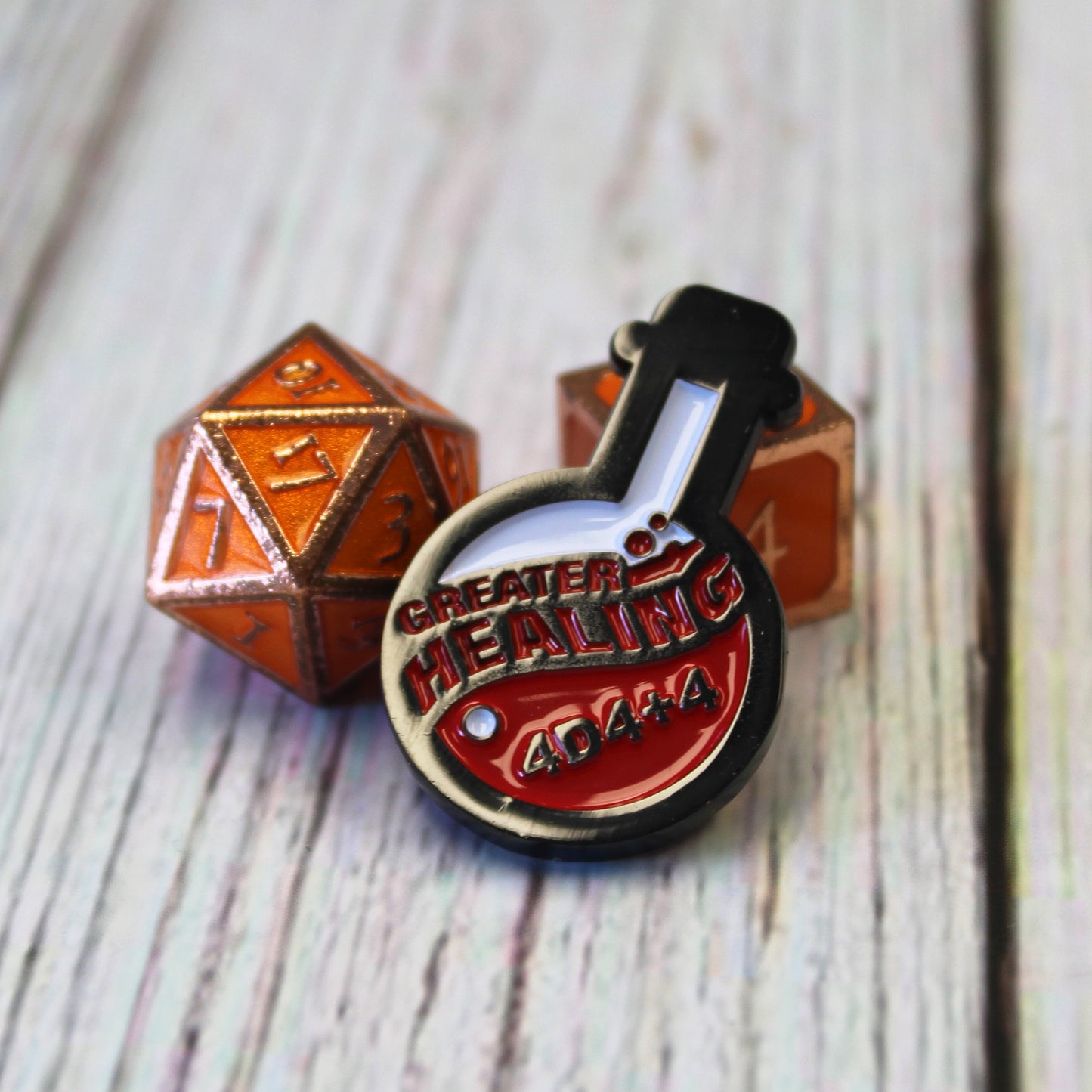 Potion of Greater Healing Token is propped up on an orange D6 die with an orange D20 die on their left, on a white wood surface.