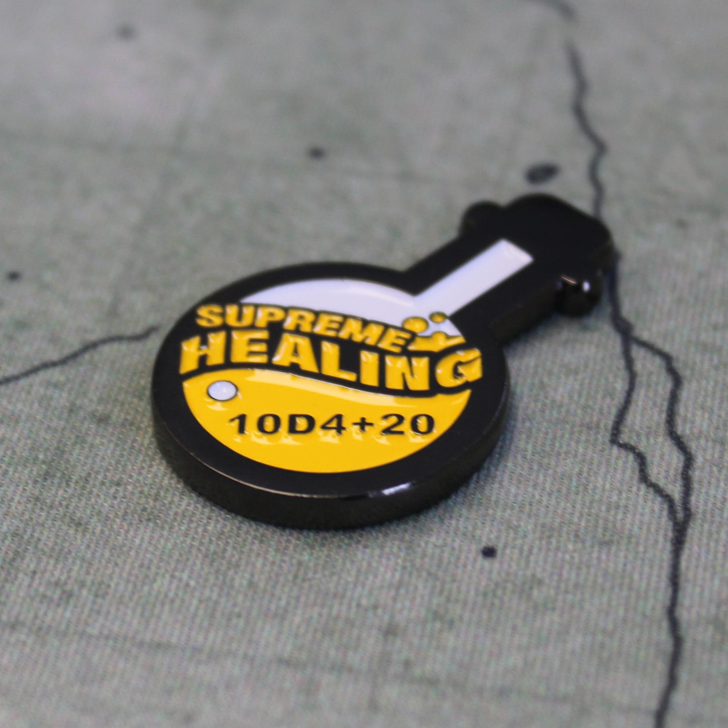 Potion of Supreme Healing Token on gray game map. Token is shaped like a round bottom boiling flask, halfway filled with the design of yellow bubbly liquid and the words "supreme healing" written in yellow. On the liquid is the black lettering "10D4+20".