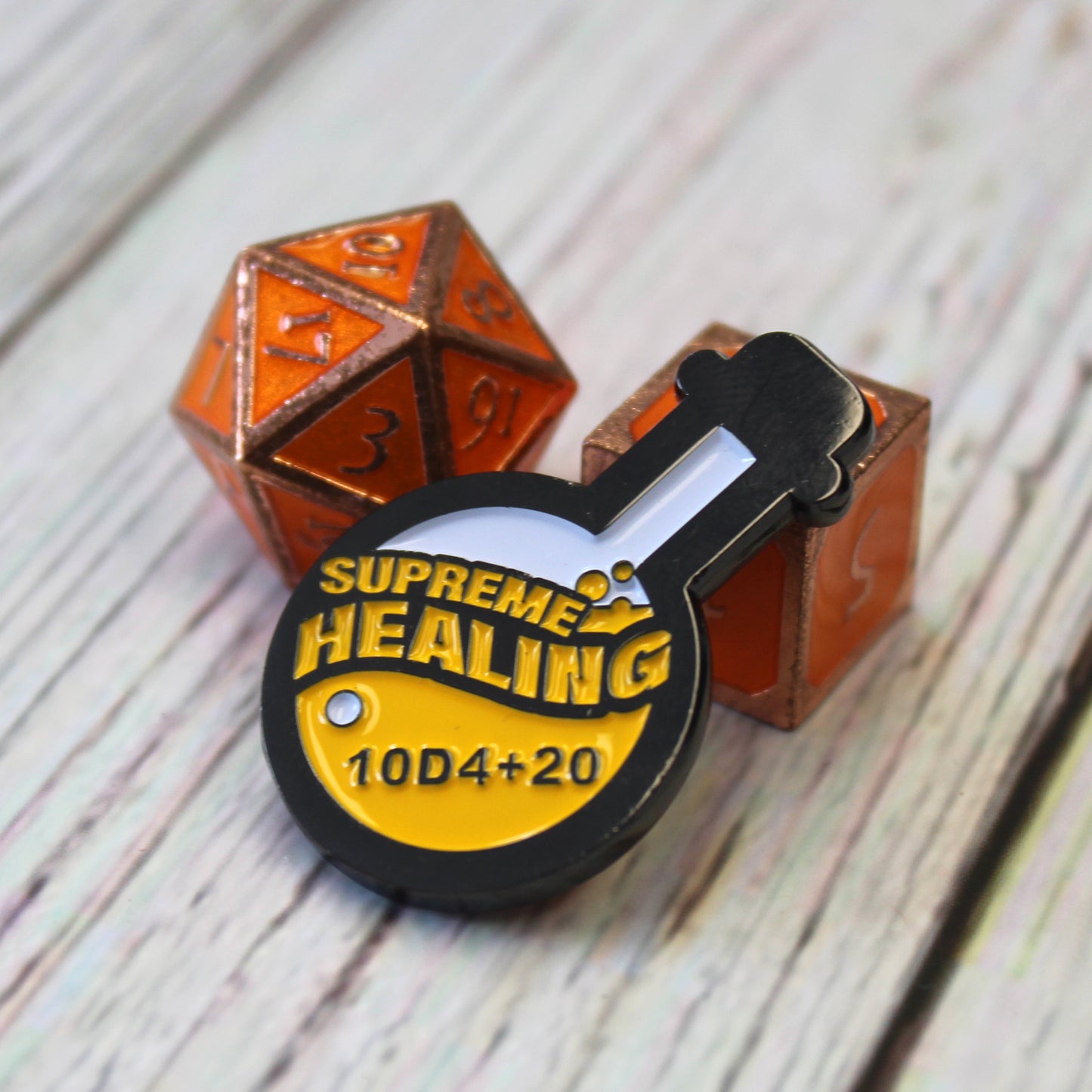 Potion of Supreme Healing Token is propped up on an orange D6 die with an orange D20 die on their left, on a white wood surface.