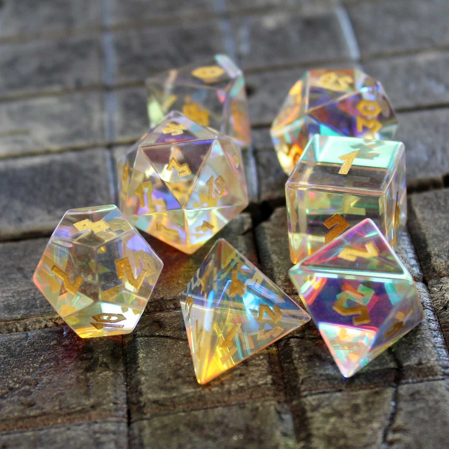 Prismatic Glass RPG dice set on a stone surface. Each die is transparent with iridescent inclusions that catch the light from every angle.