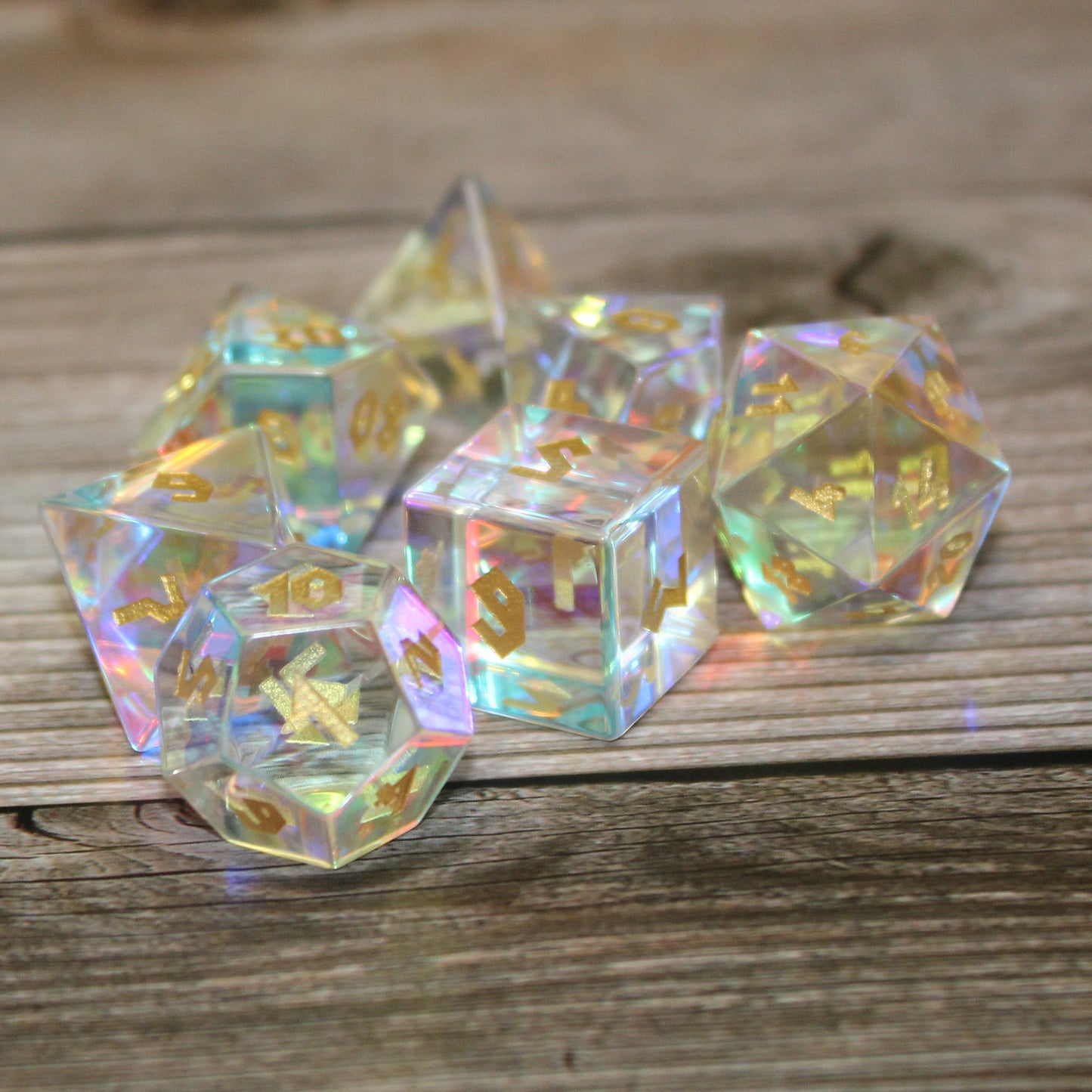 Close up photo of Dice Dungeons' Prismatic Glass dice set on a wooden surface with the d12 in the foreground showing the 1 face to the viewer. This set is transparent with shimmering inclusions in each to refract light.