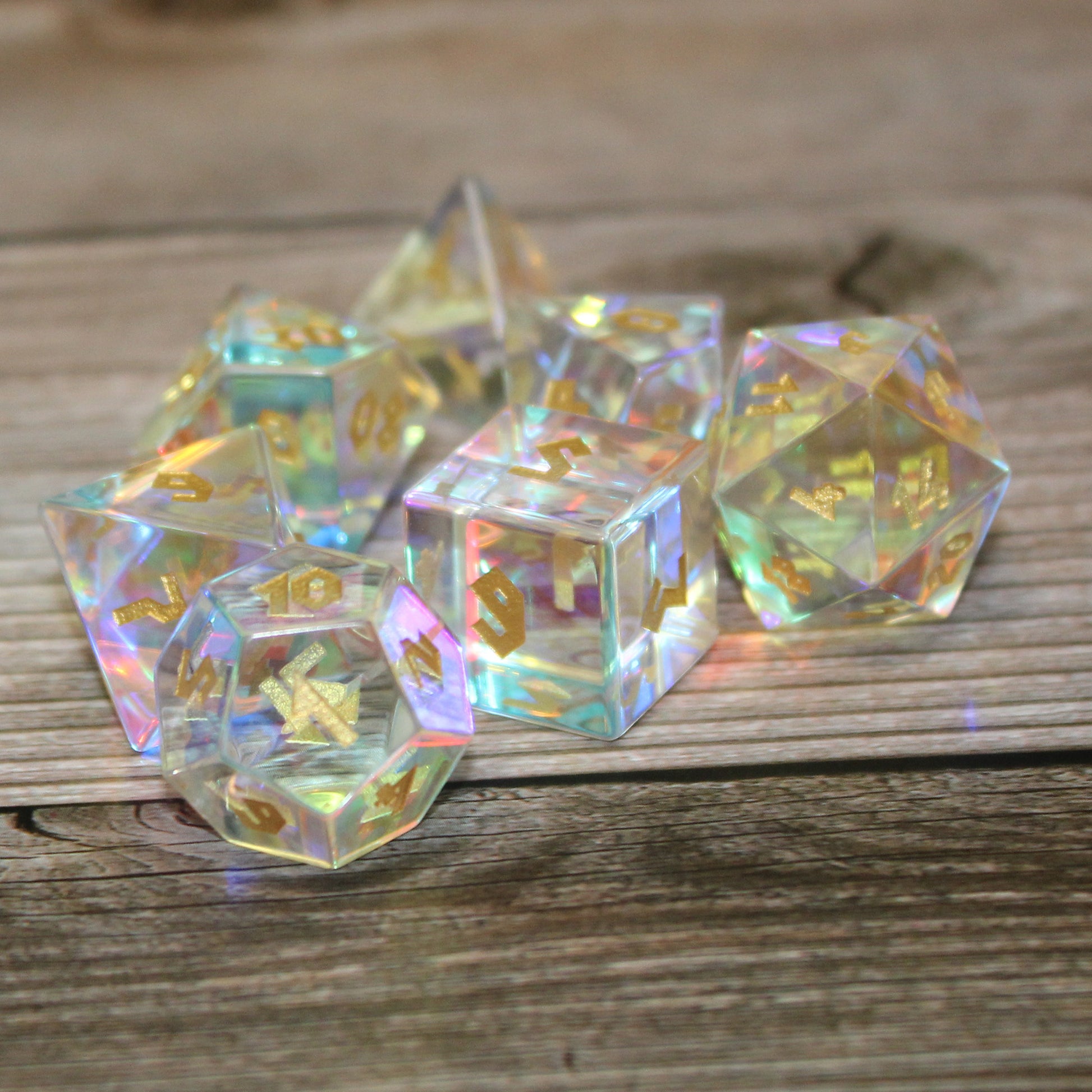 Close up photo of Dice Dungeons' Prismatic Glass dice set on a wooden surface with the d12 in the foreground showing the 1 face to the viewer.  This set is transparent with shimmering inclusions in each to refract light.