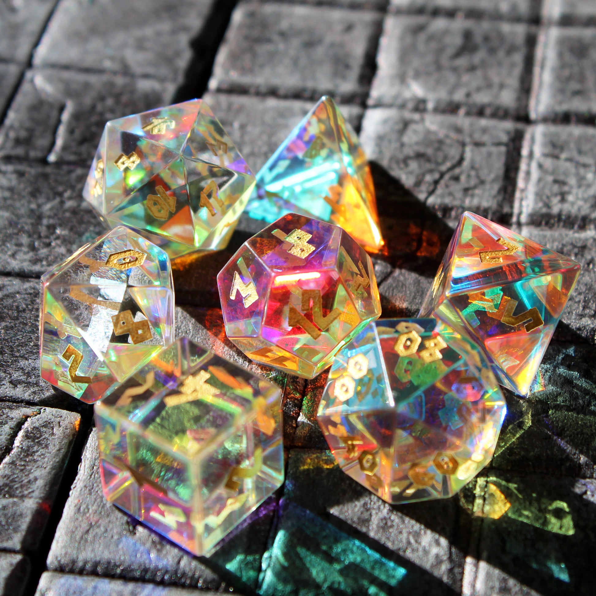 Sunlight shining through Dice Dungeons' Prismatic Glass RPG set arranged on a stone terrain tile.  The holographic inclusions within each die refract light in a unique and pleasing way.
