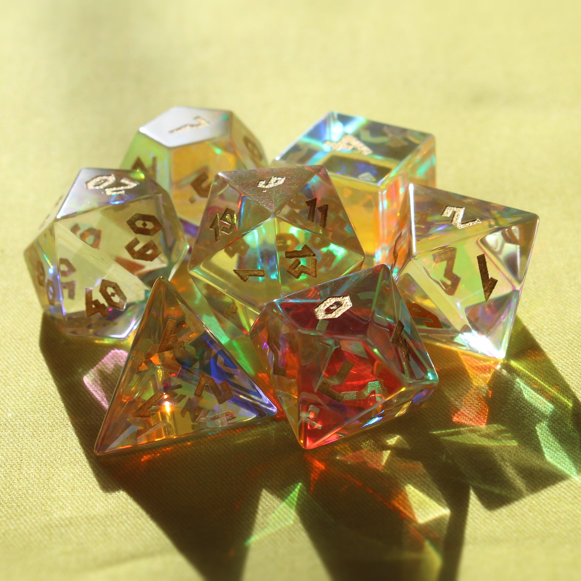 Dice from the Prismatic Glass set arranged in a group on a yellow surface with sunlight refracting through the shadows cast towards the viewer.