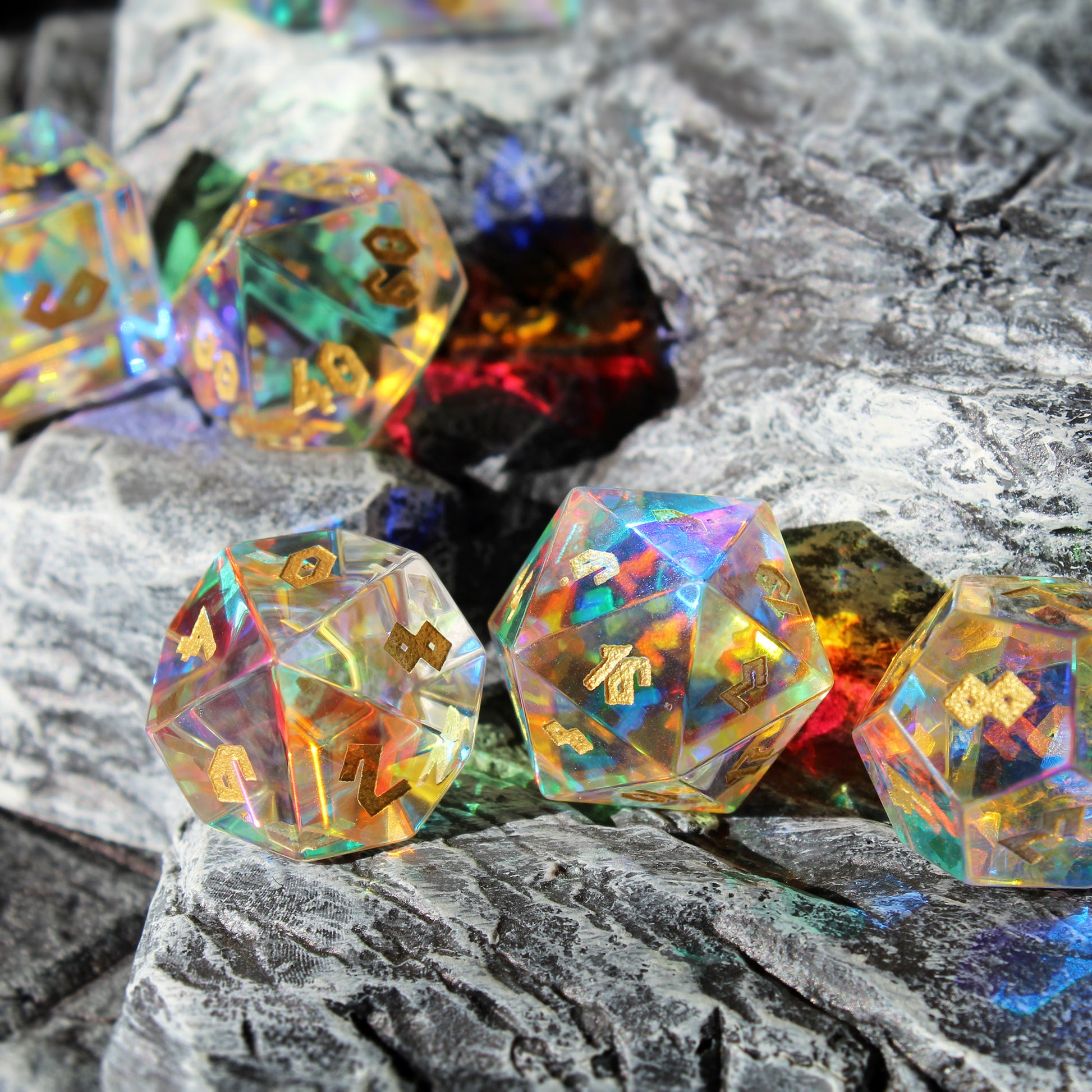 Prismatic Glass dice arranged with light shining through the dice on a piece of stone scatter terrain with the d10, d20, and d12 in the foreground. The chiseled font is inlaid with an antique gold coloring for legibility.