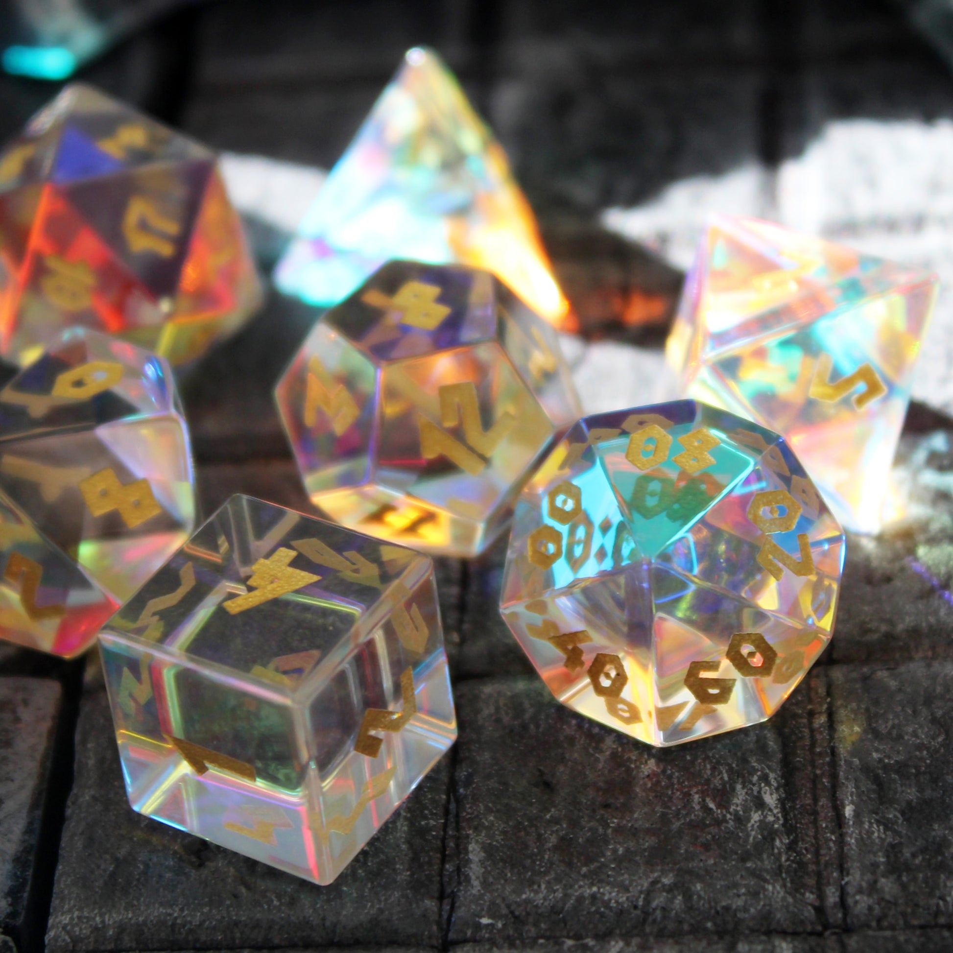 Close up detail of Prismatic Glass dice on a stone surface with the d6 in the foreground showing the 4 face. Light refracts through the dice for a unique beauty.