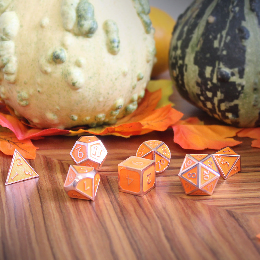 Imperial pumpkin dice set arranged on a wooden surface, with fabric fall leaves and green and white ornamental gourds behind them.