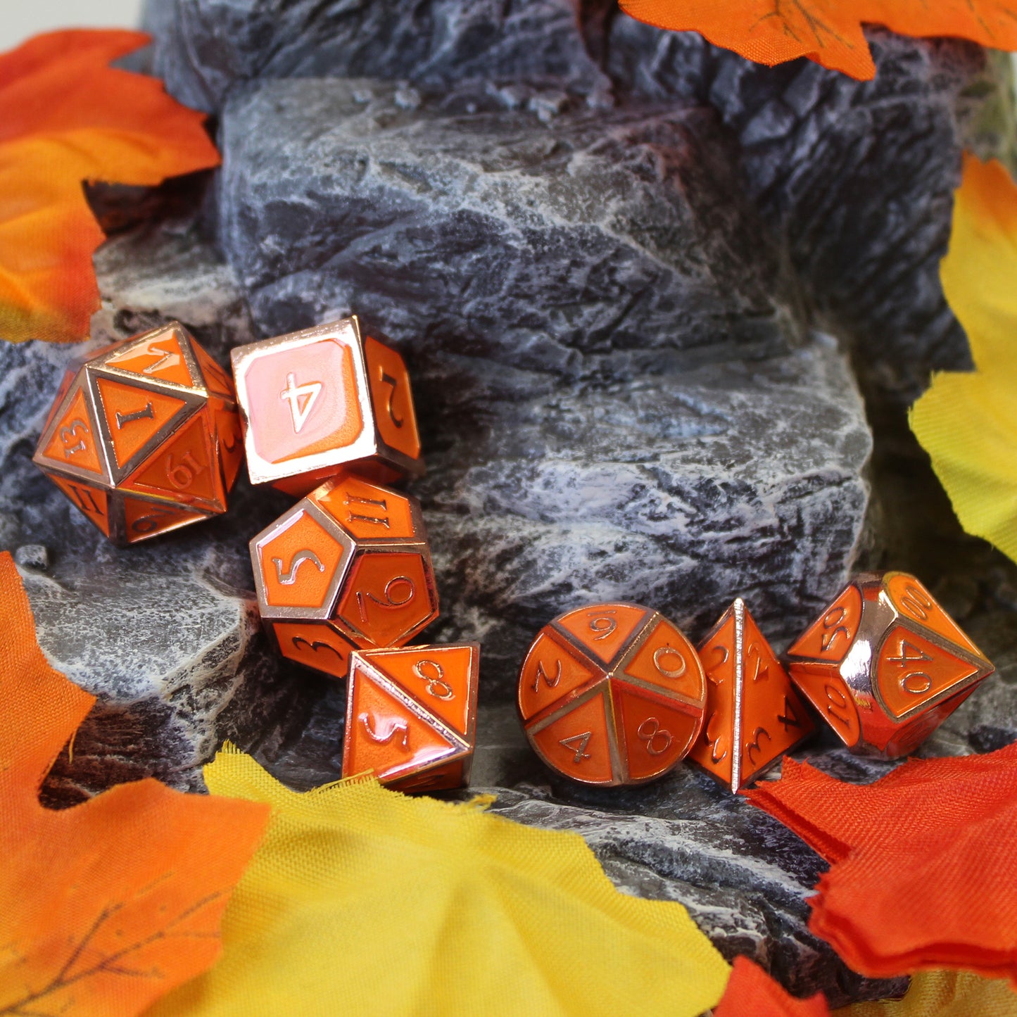 Imperial Pumpkin dice set scattered on a rocky set piece, surrounded by fabric fall leaves.