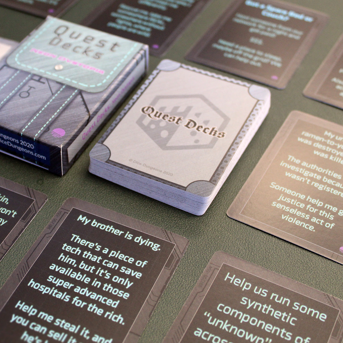 A stack of cards with the top card labeled "Quest Decks" laid on a black table surrounded by small stacks of cards from the deck in a uniform grid across the table. The Neon Dystopia Quest Deck box is directly to the left of the central stack of cards.